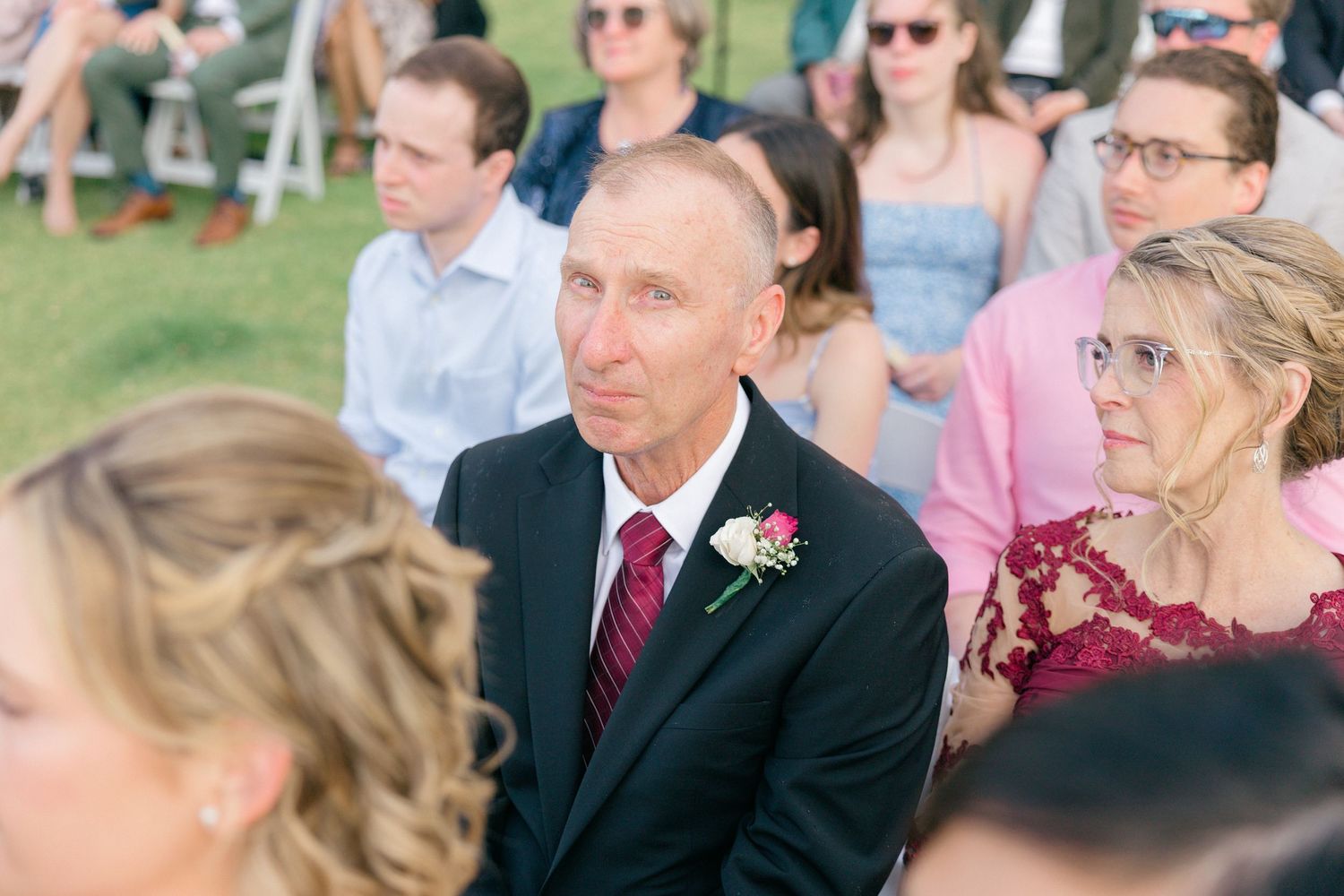 Wedding guests in formal attire gather outdoors for a ceremony with palm trees in the background.