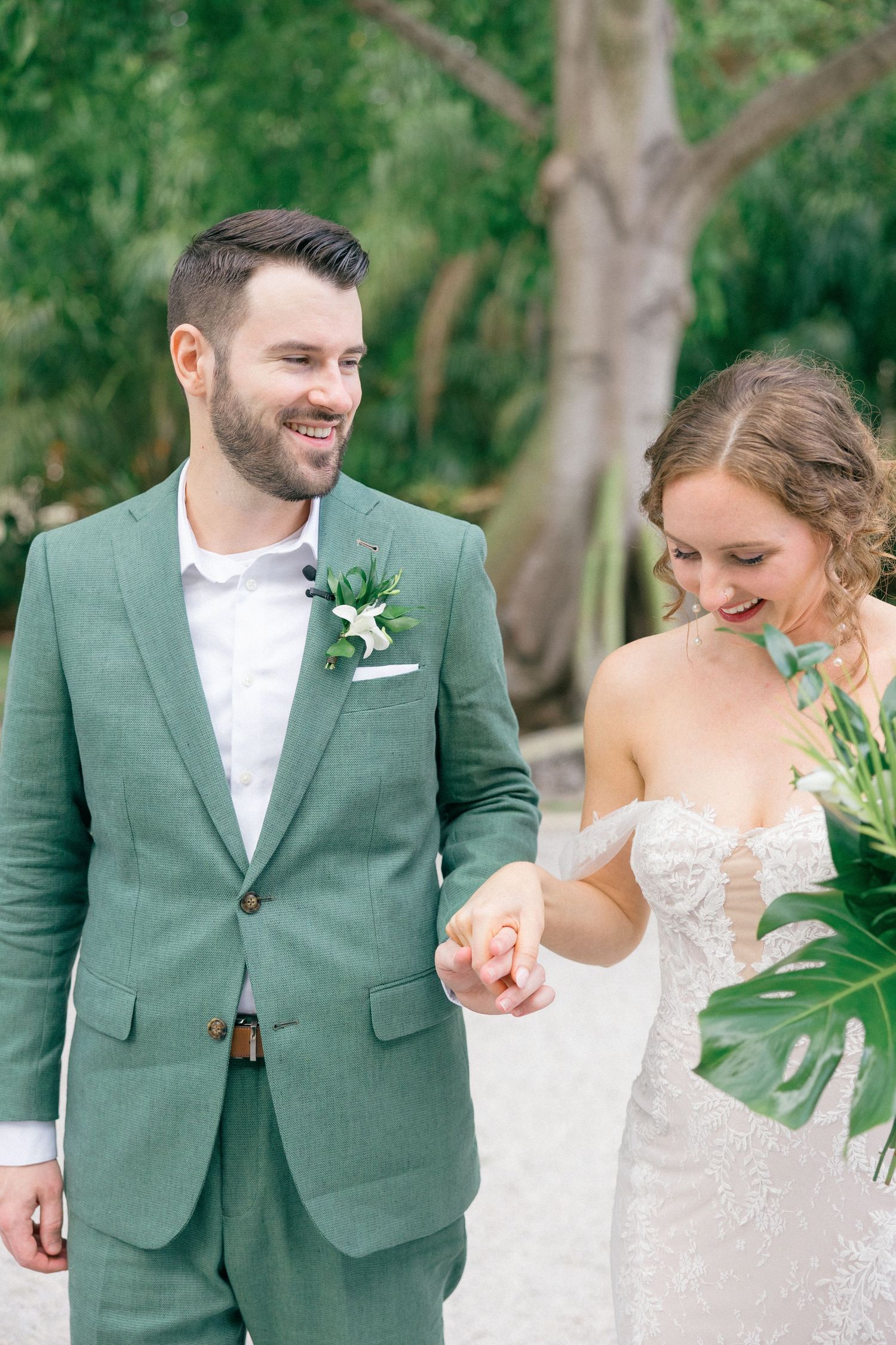 Newlyweds sharing joyful moments in a garden setting with the groom wearing a sage green suit.