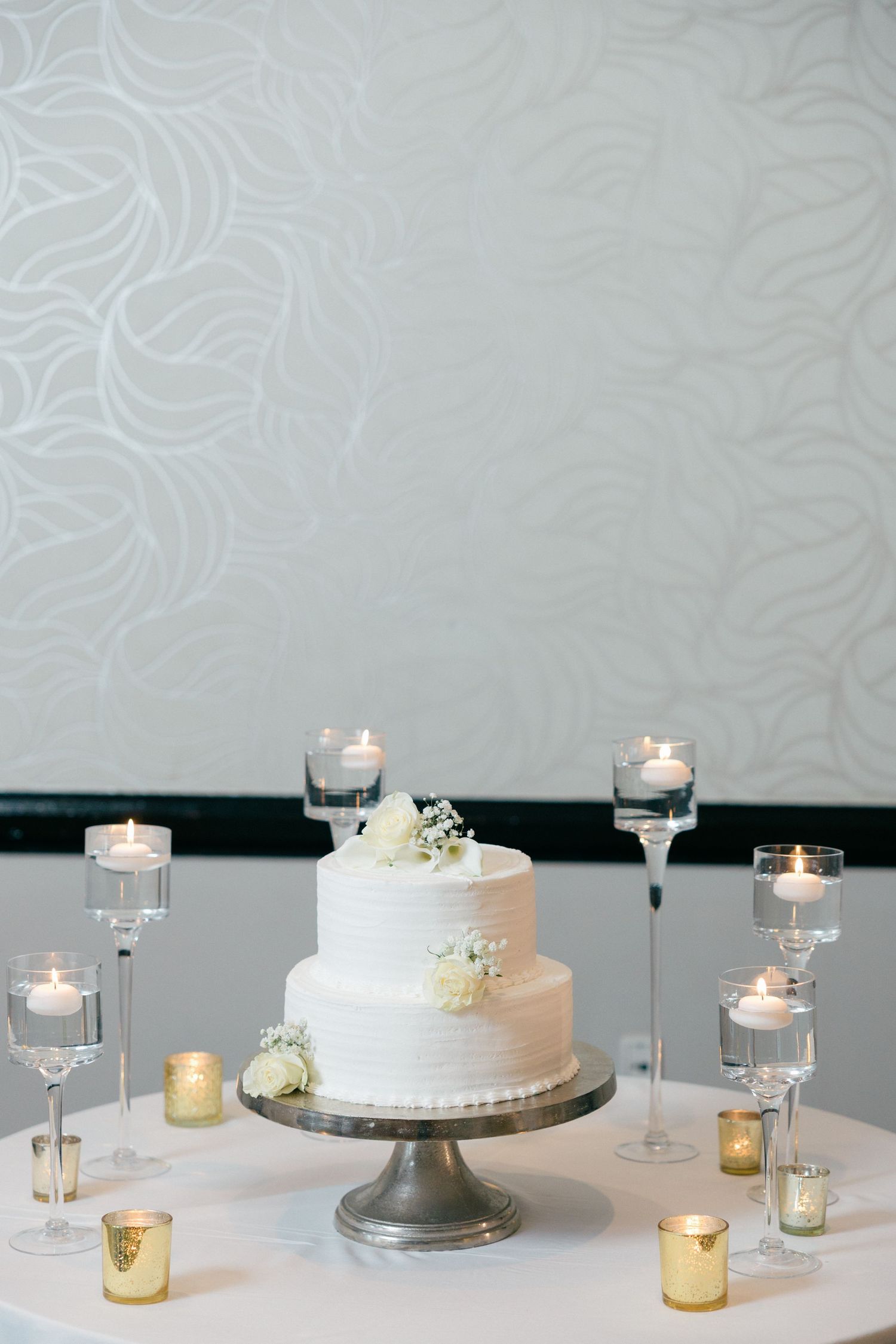 Simple white wedding cake display with candlelight and minimalist table decorations.