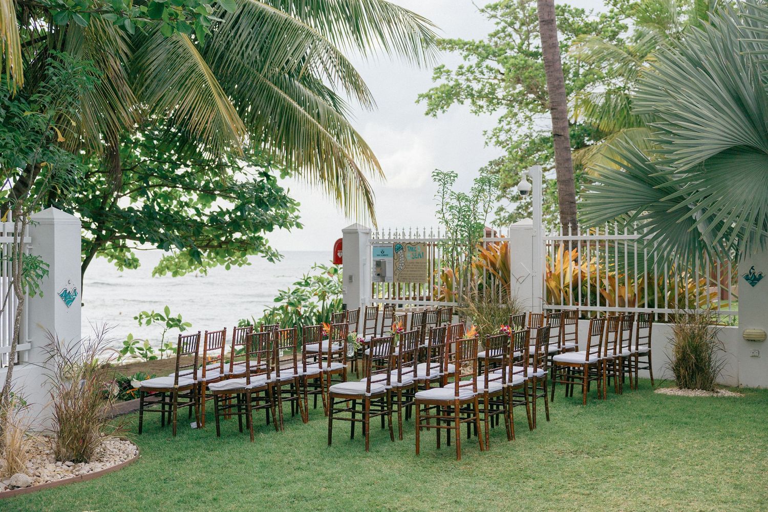 Panoramic view of an outdoor wedding venue with rows of chairs and tropical landscaping.