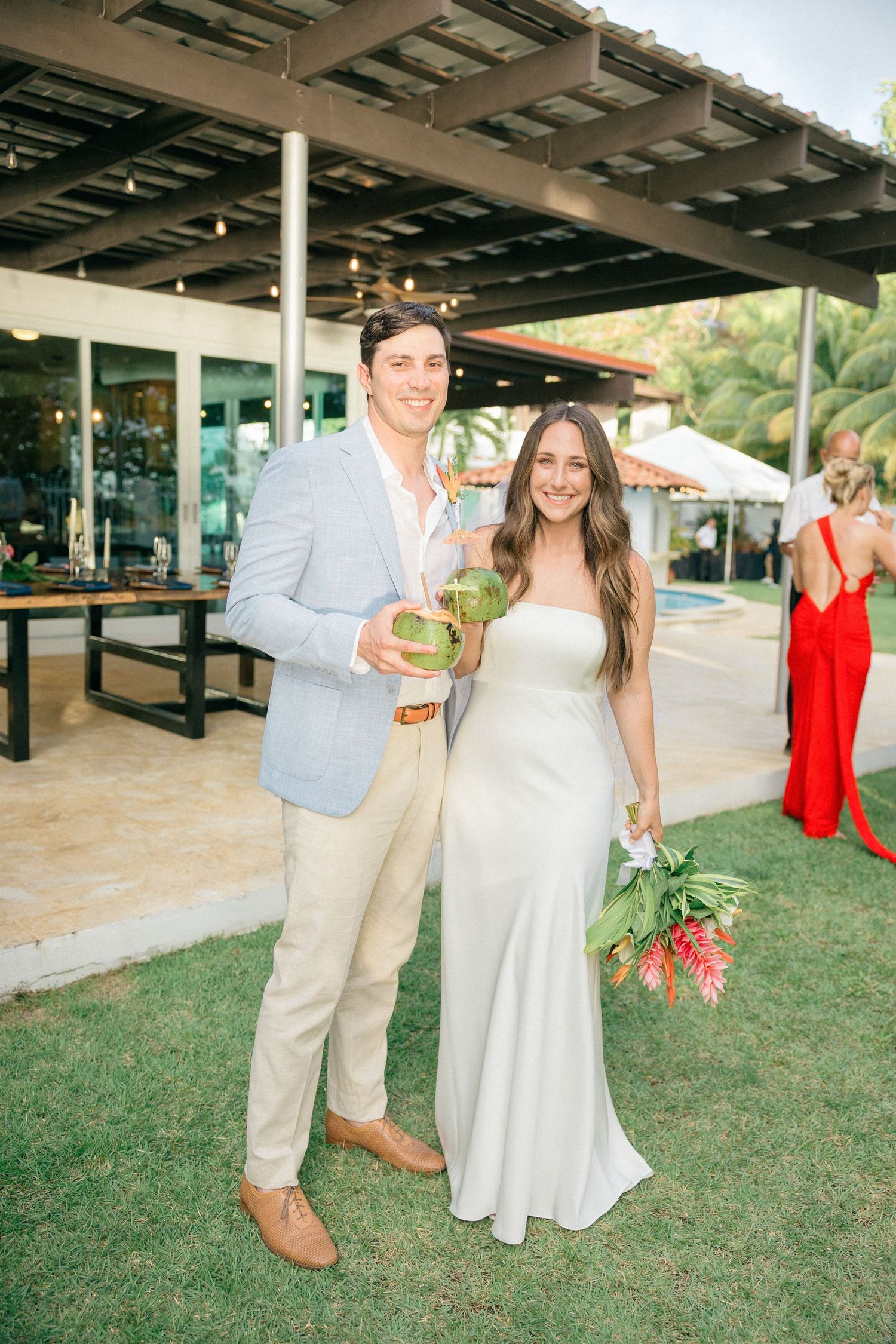 A couple at a tropical wedding reception holding a coconut drink.