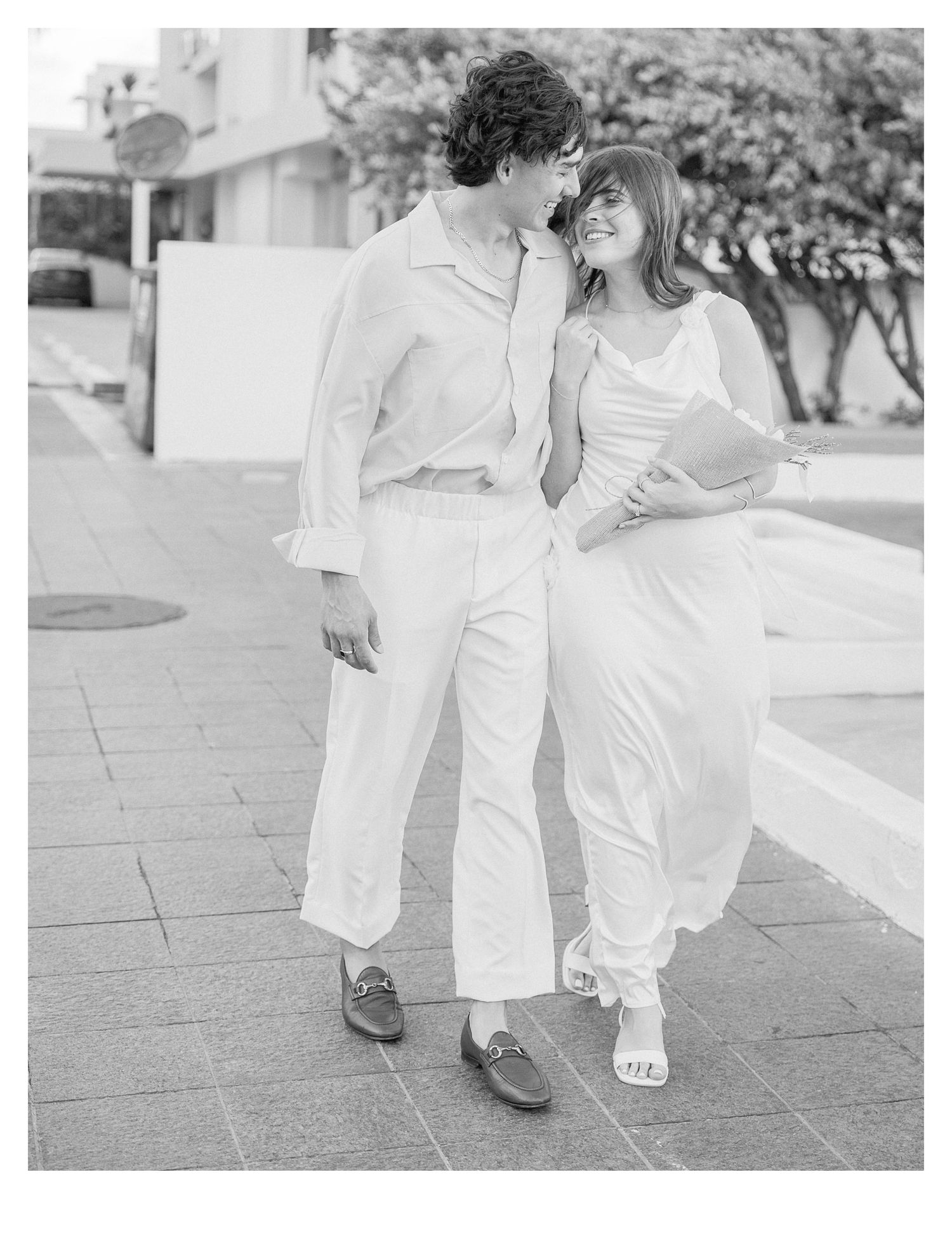 Couple strolling hand in hand on a stone walkway in coordinated white attire.