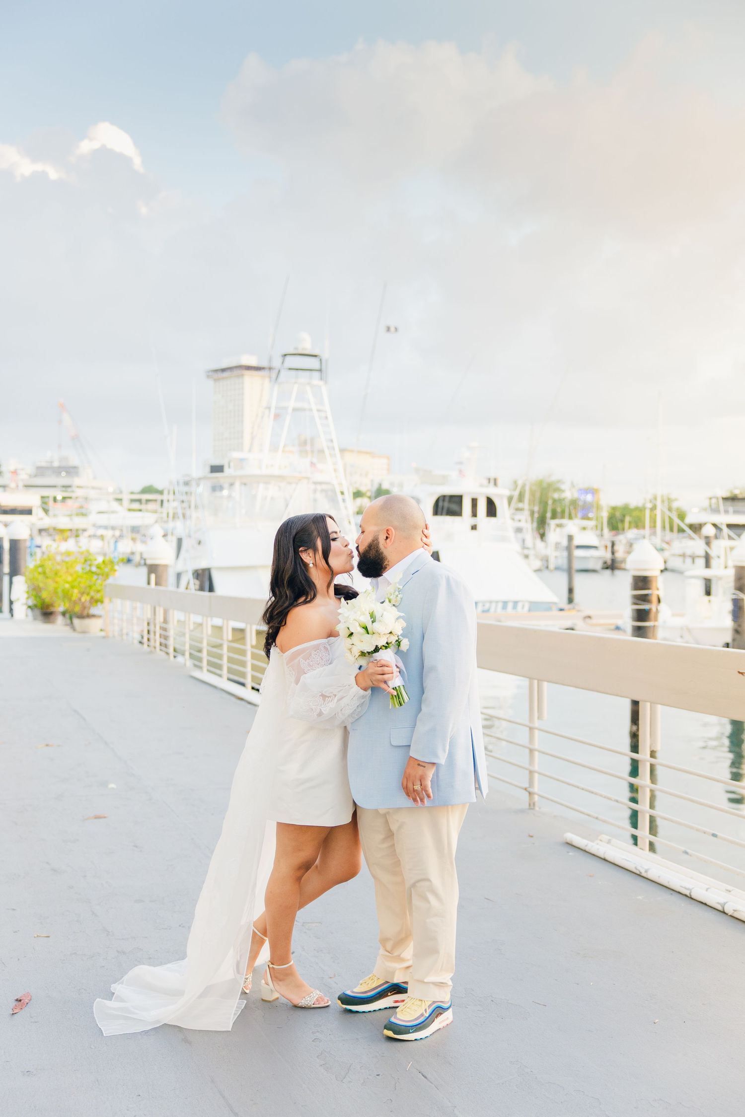 Wedding couple sharing a romantic moment on a marina dock with boats in the background.