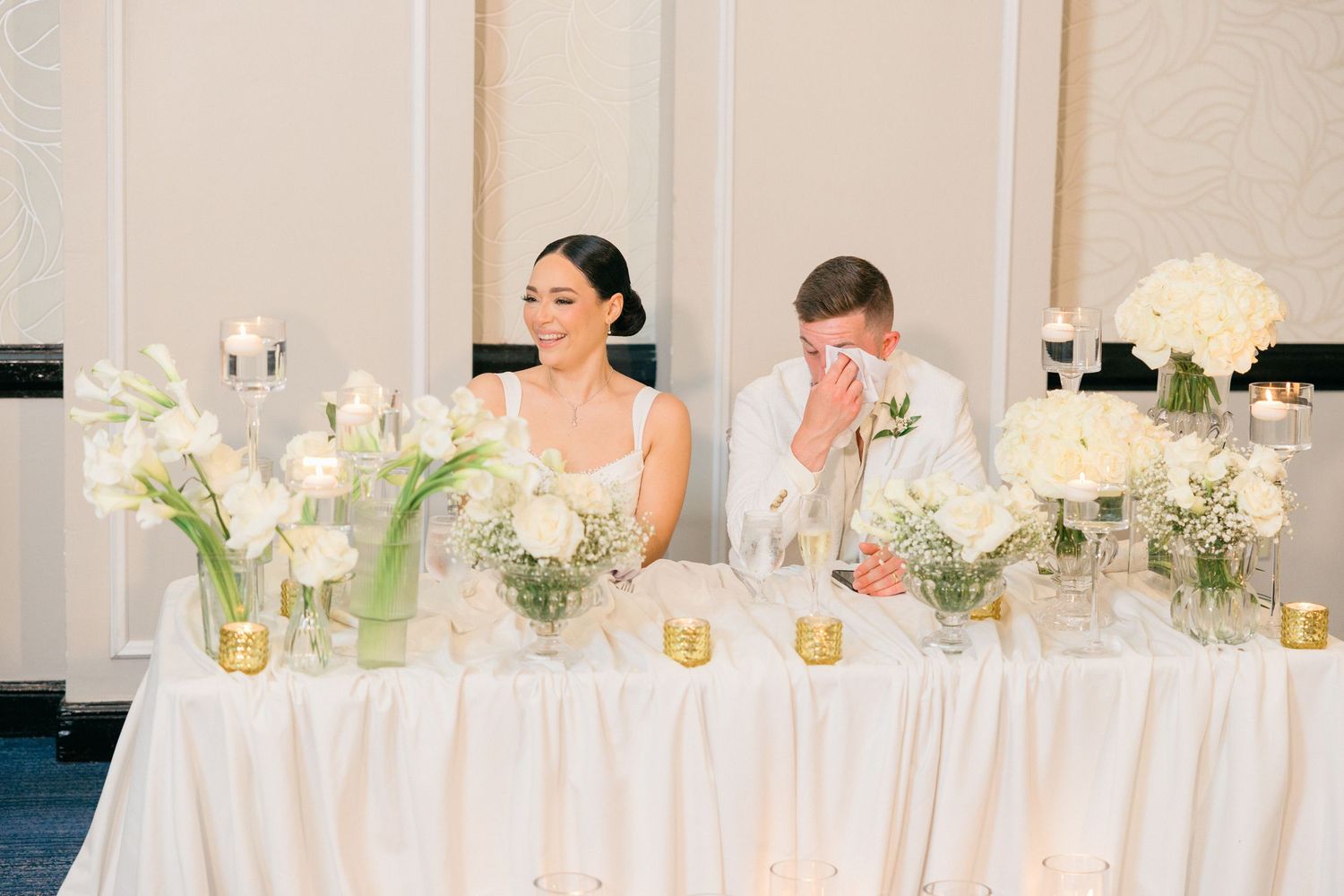 Elegant wedding reception table decorated with white floral centerpieces and glowing candles.
