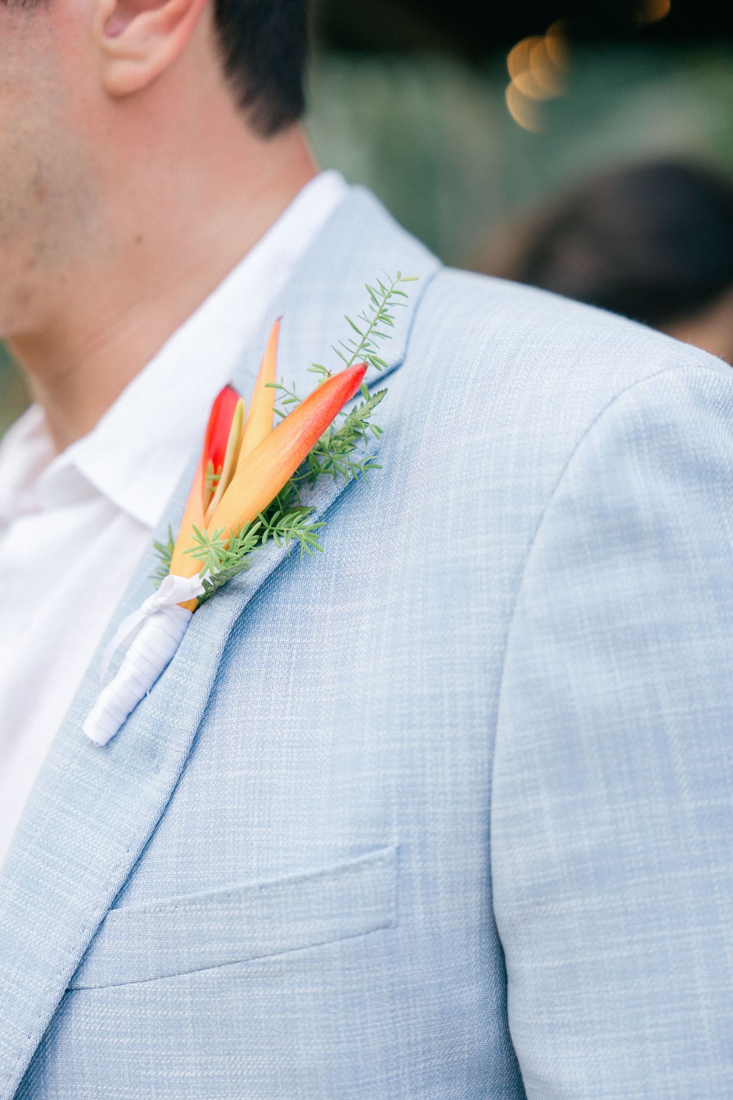 Close-up of an orange tropical flower boutonniere on a light blue suit jacket.