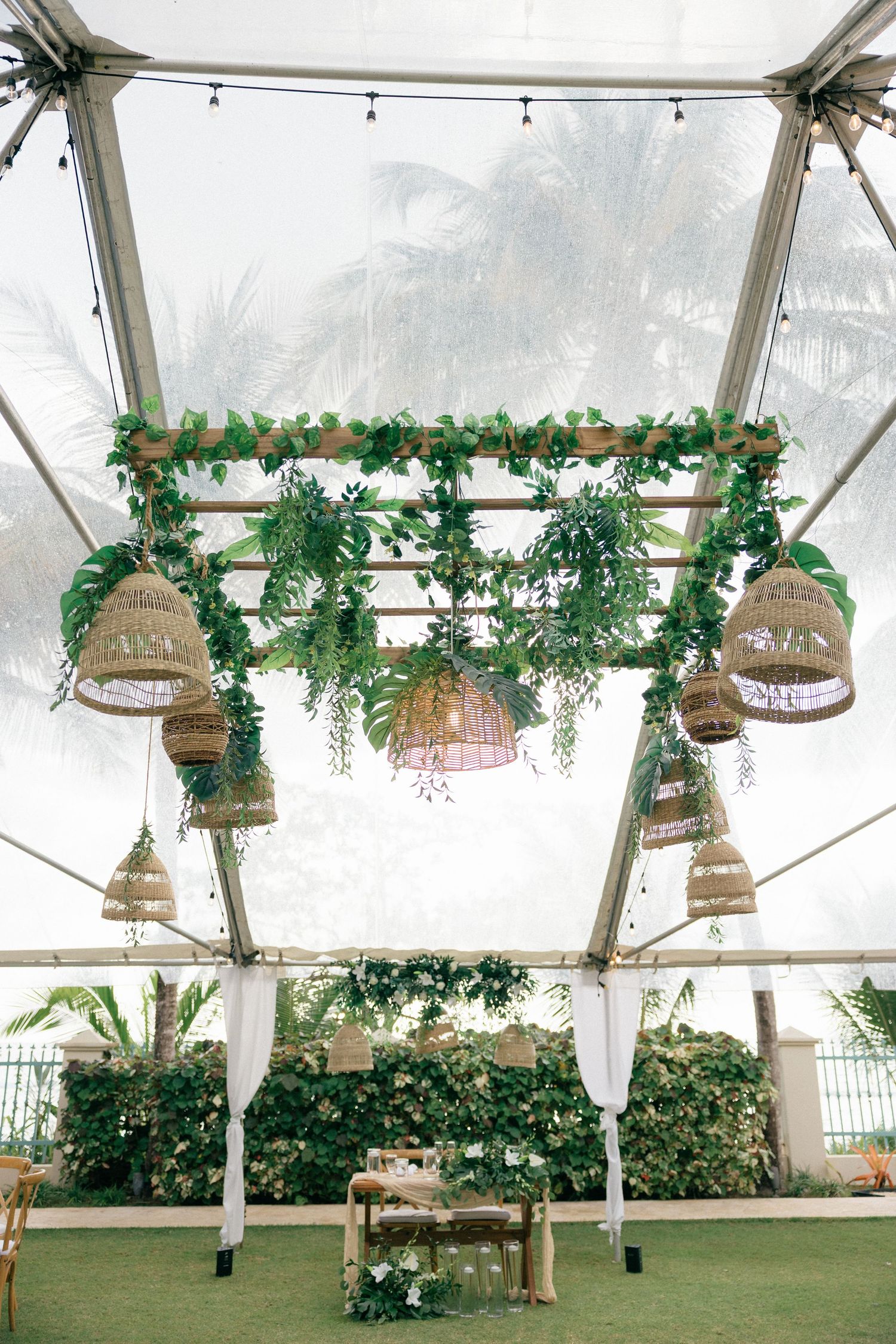Tent ceiling decorated with hanging wicker baskets and lush greenery garlands.