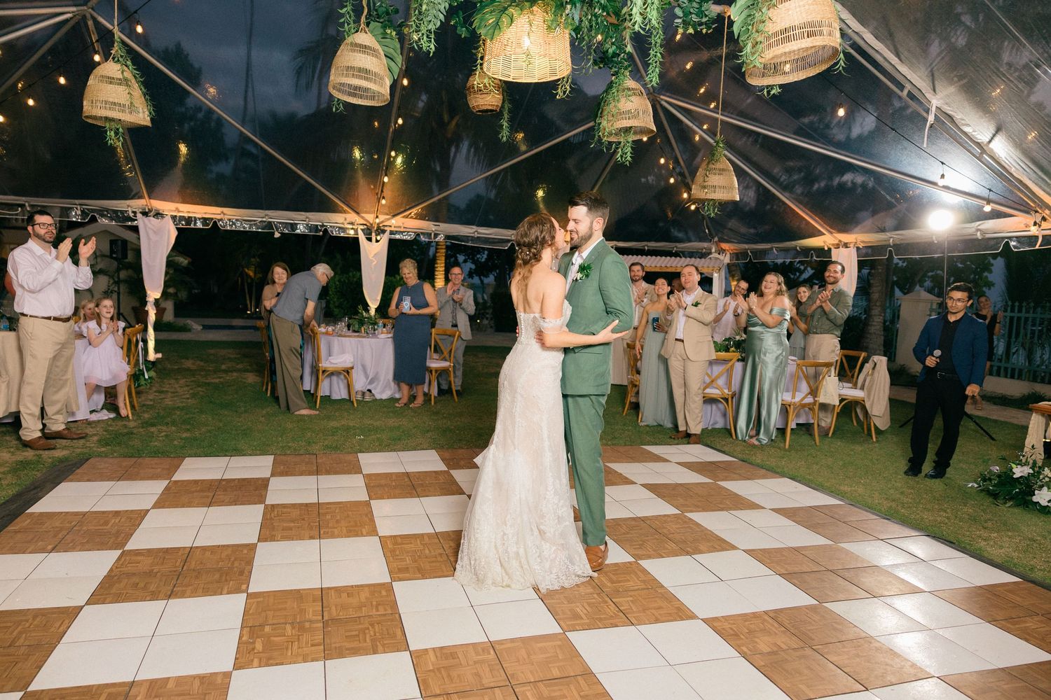 Wedding reception dance floor under a tent with hanging lantern decorations and checkered flooring.