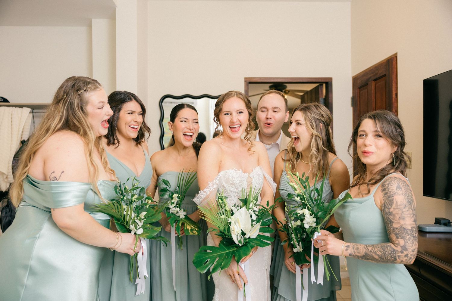 Bridal party wearing mint green gowns pose together while holding matching greenery bouquets.