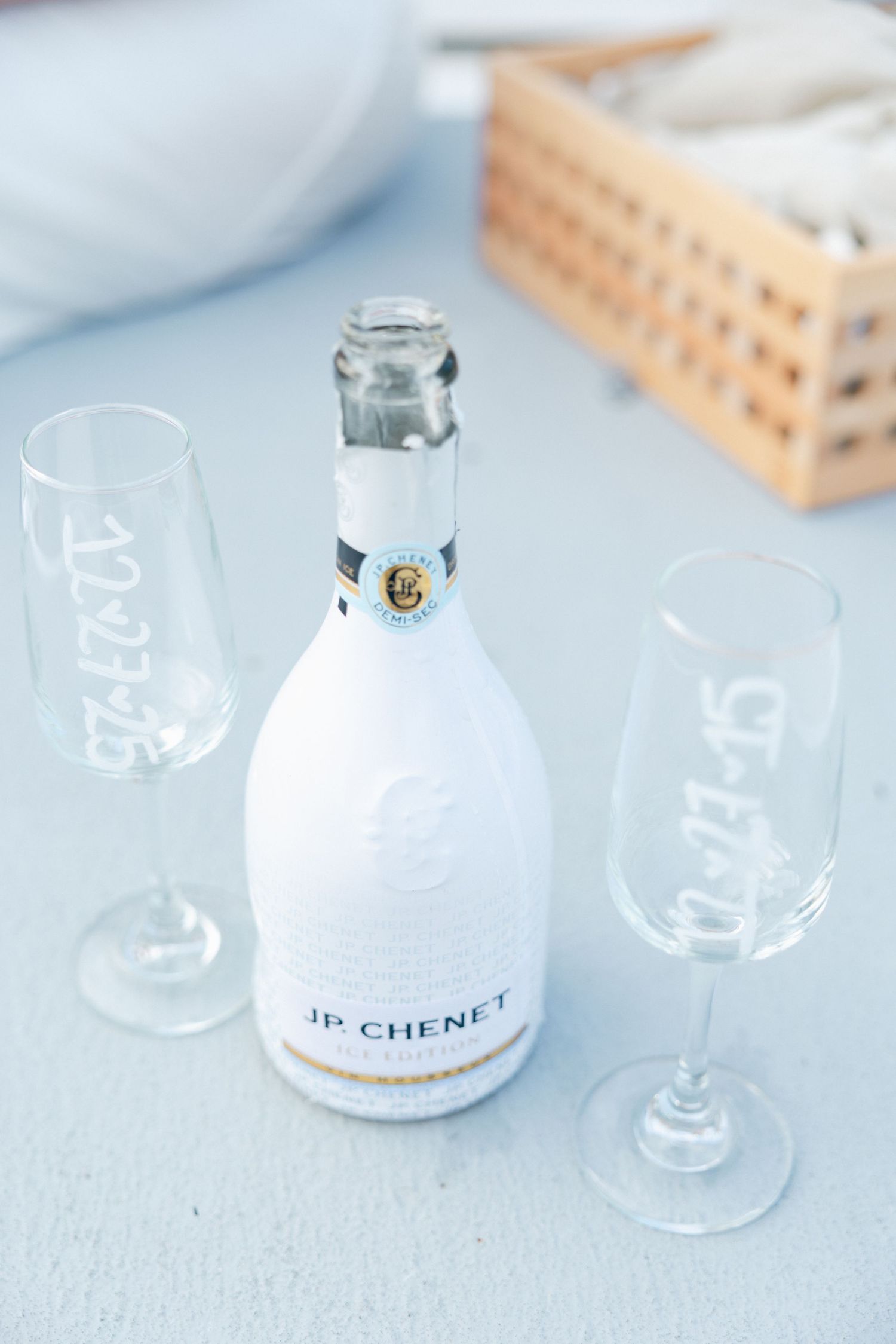 Wine glasses and a bottle of JP Chenet arranged on a light blue surface.