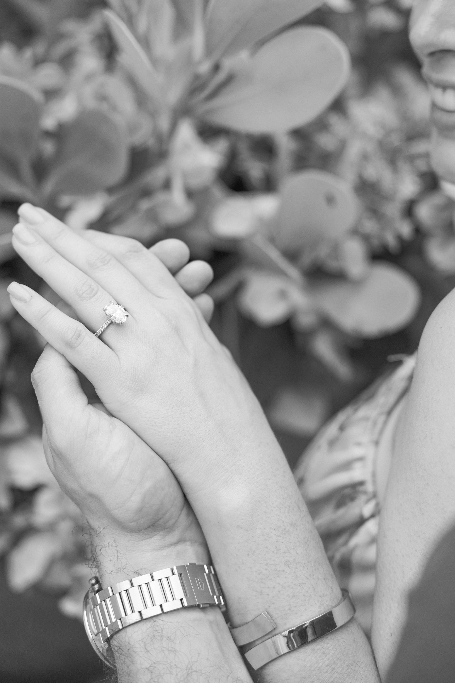 Close-up black and white photo of hands showing engagement ring and watch details.