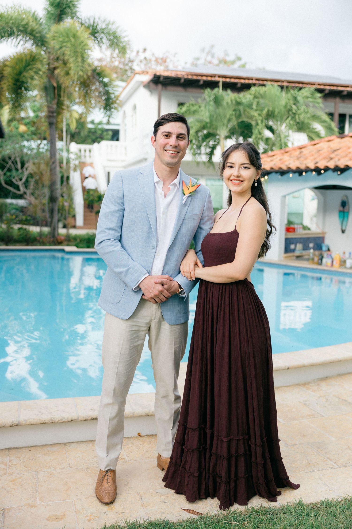 Couples posing for photos beside a resort swimming pool in formal attire.