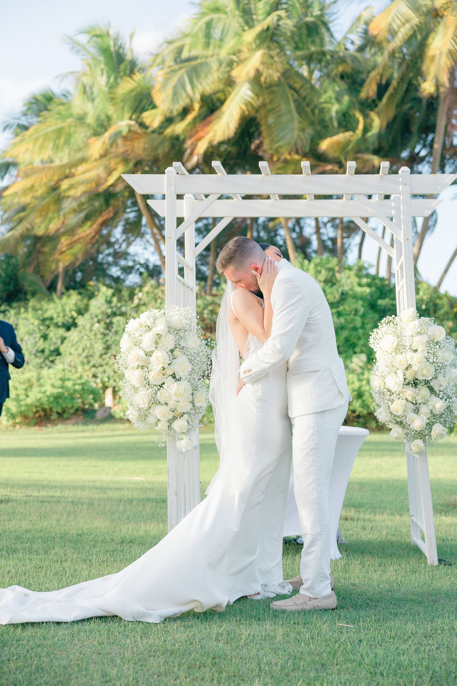 Beachside wedding ceremony with white decor and tropical palm trees in the background.