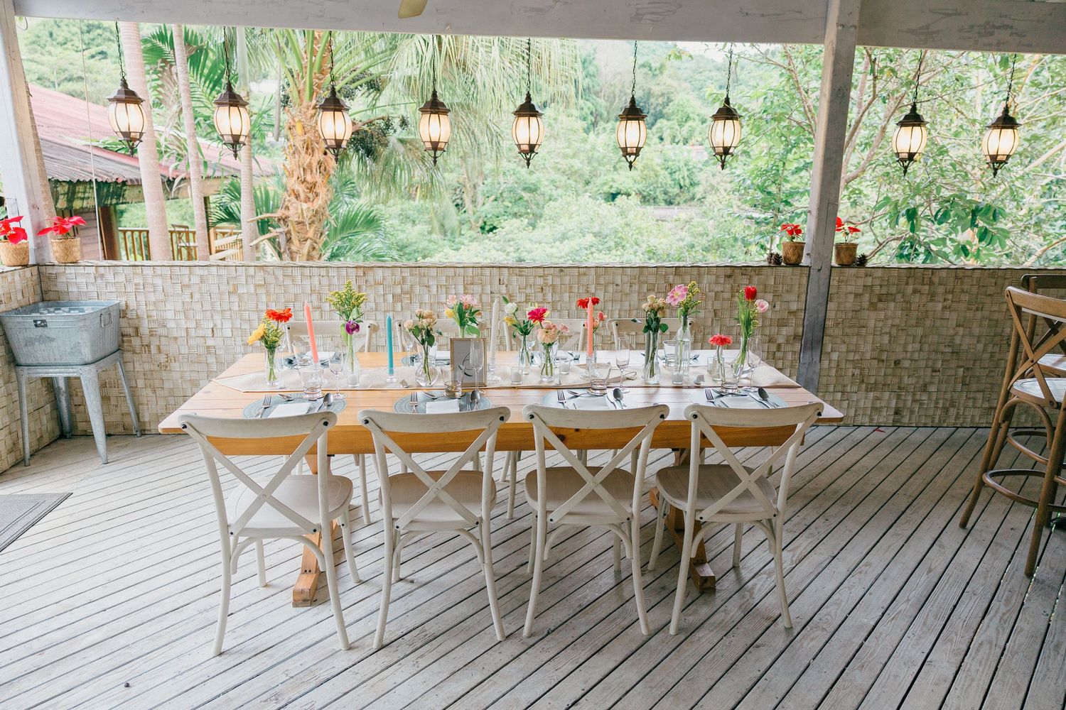 Outdoor wedding reception setup with wooden tables and hanging lights under covered patio.