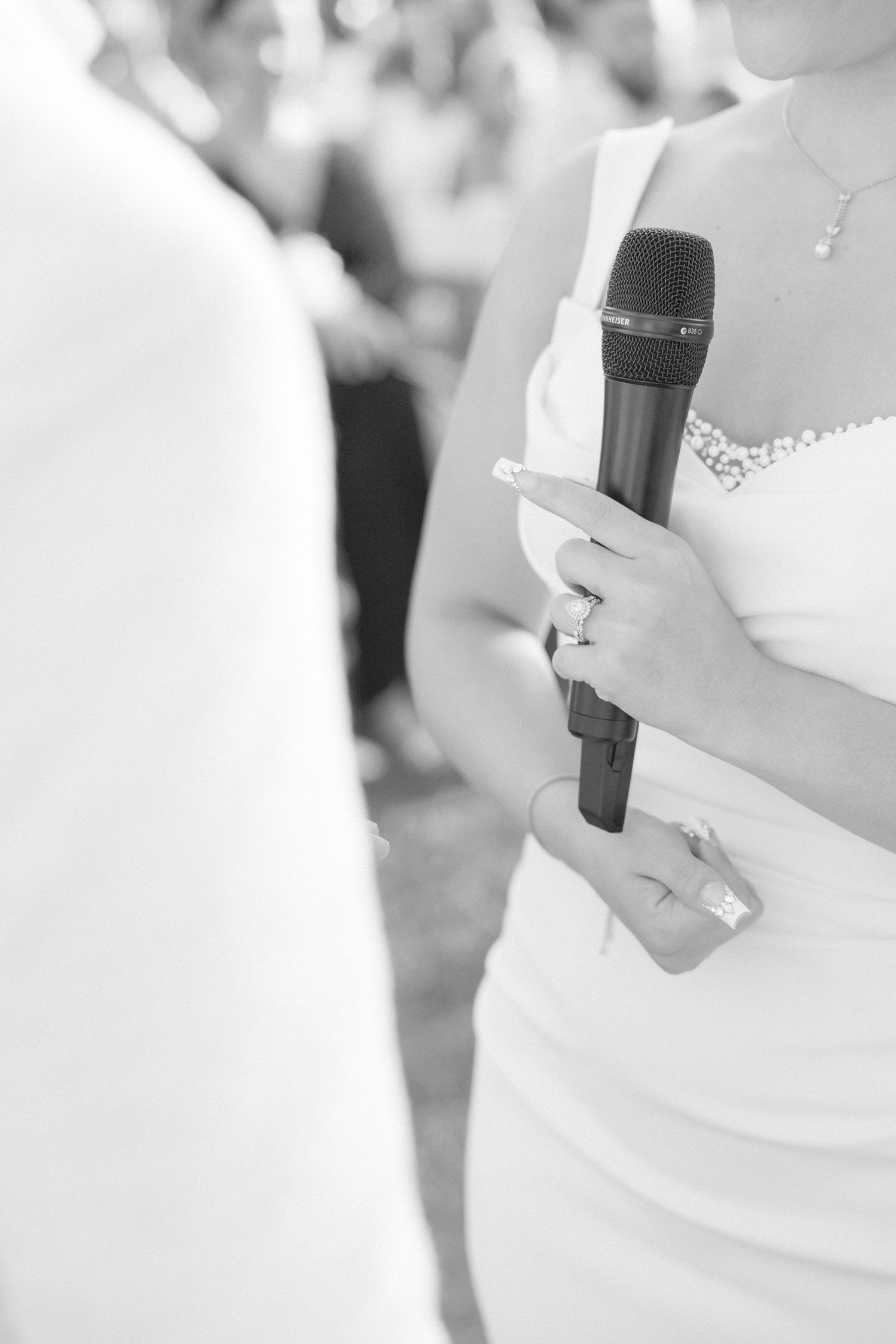 Close-up of hands holding a microphone during an outdoor wedding ceremony.