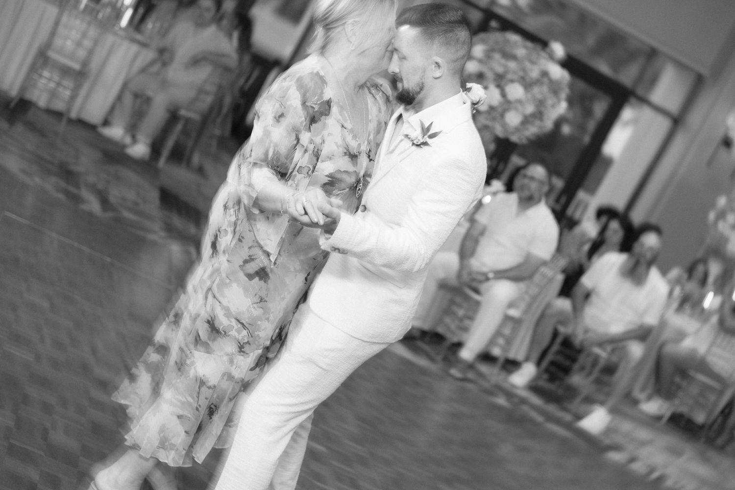 Black and white photo shows couples dancing at an elegant indoor wedding celebration.