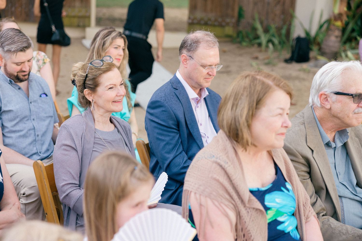 Wedding guests watching ceremony from wooden chairs at outdoor venue.