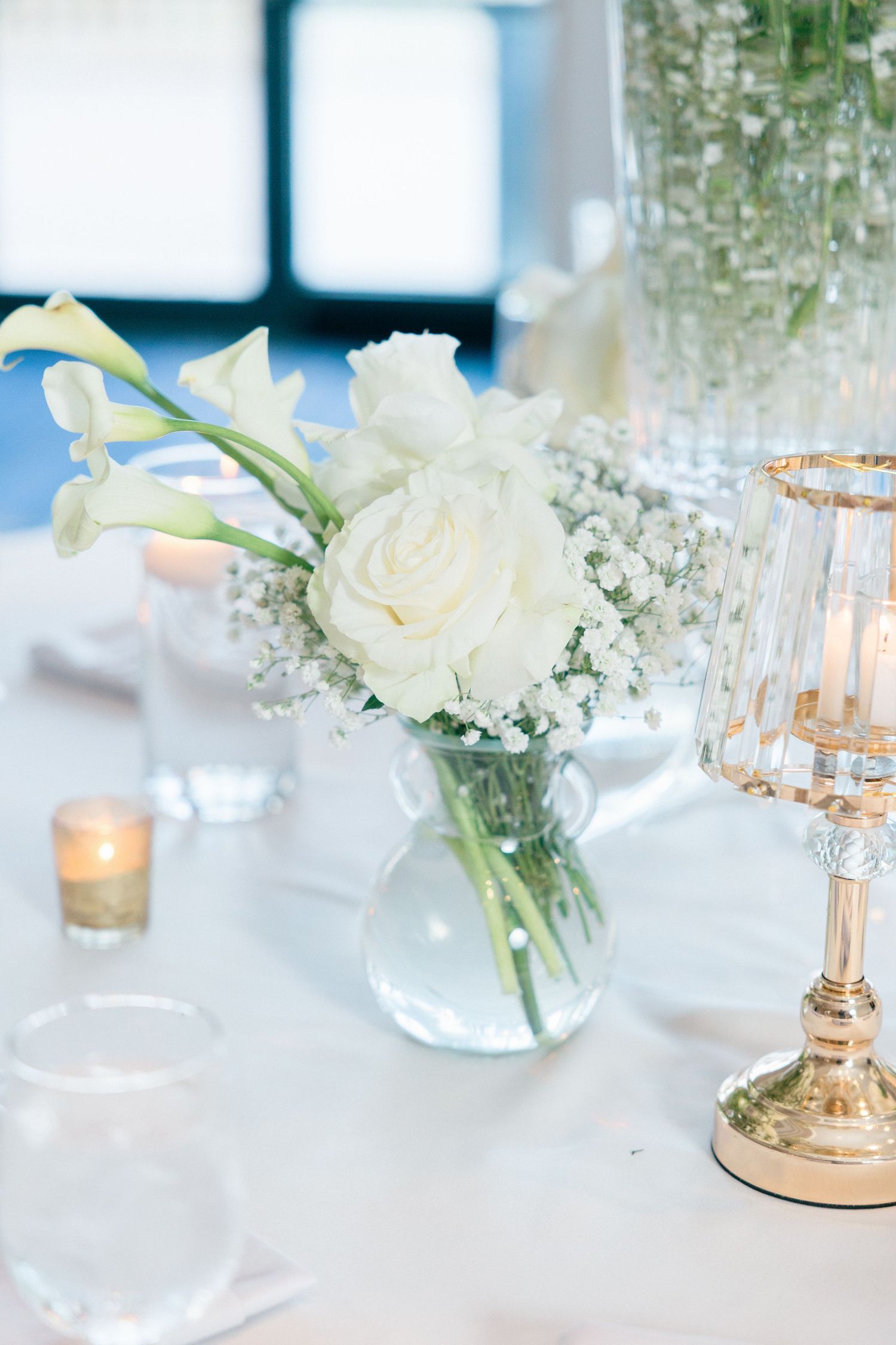 Elegant wedding reception table with white roses and glowing candles in glass holders.