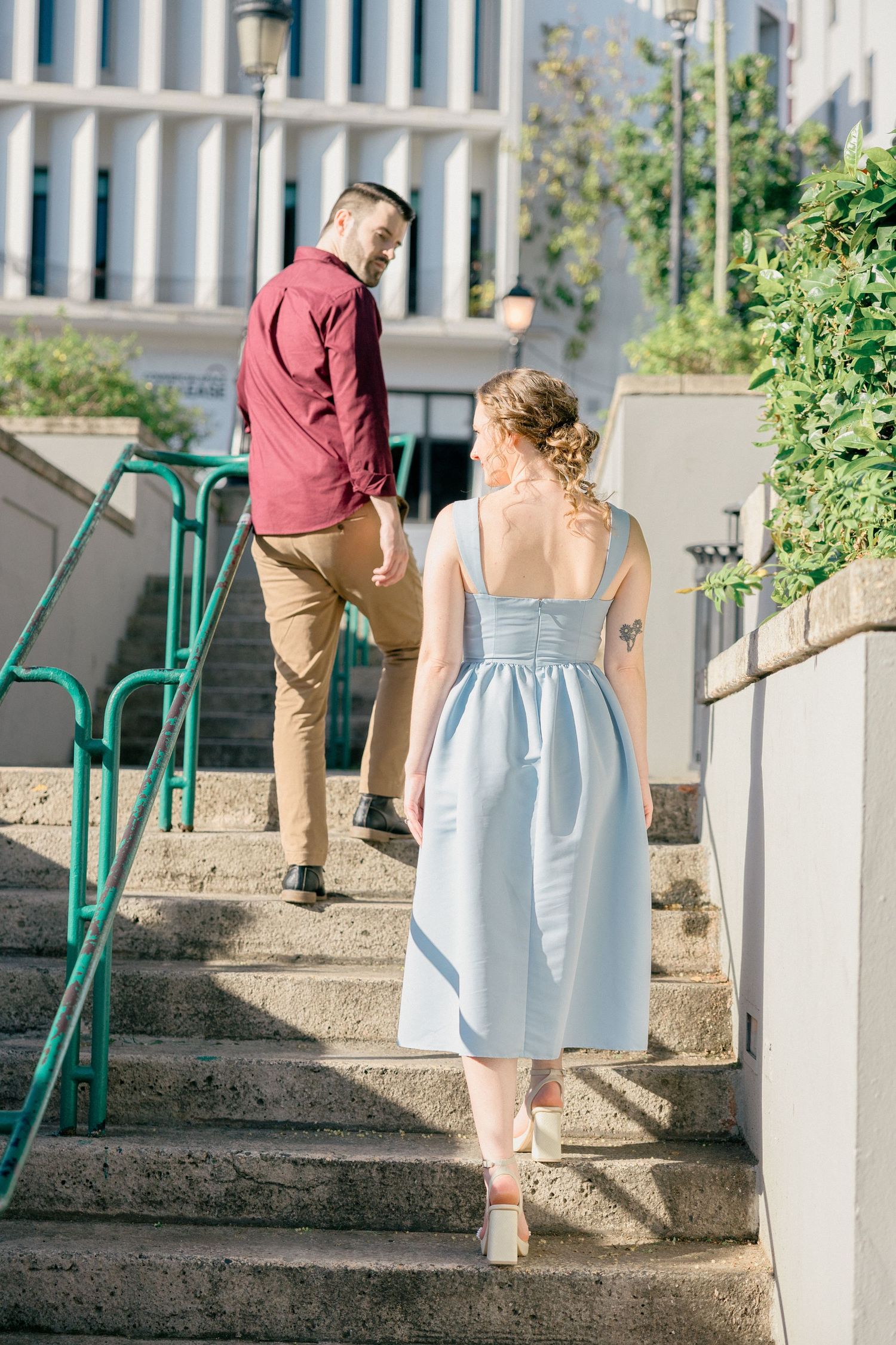 Couple walking up concrete steps with green railings at an outdoor venue.