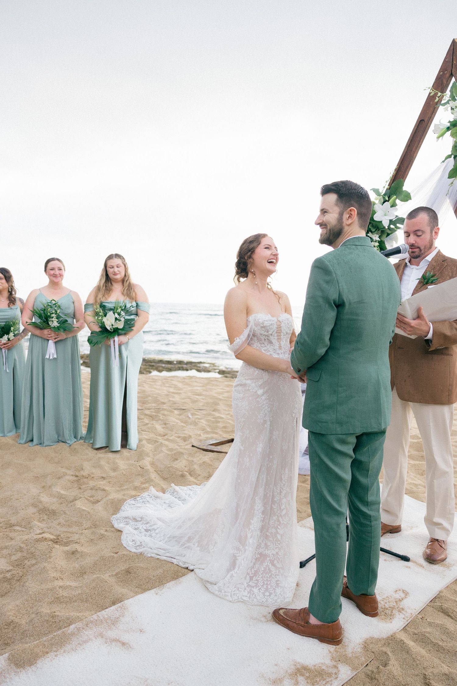 Wedding ceremony on beach with bridal party in seafoam green dresses.