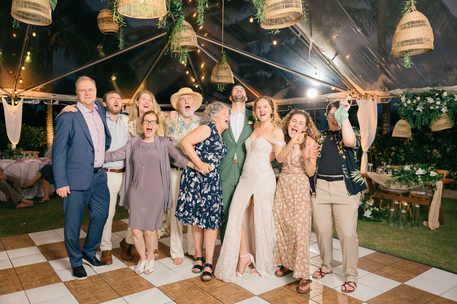 Wedding guests dancing and celebrating under a tent with decorative lanterns and a checkered dance floor.