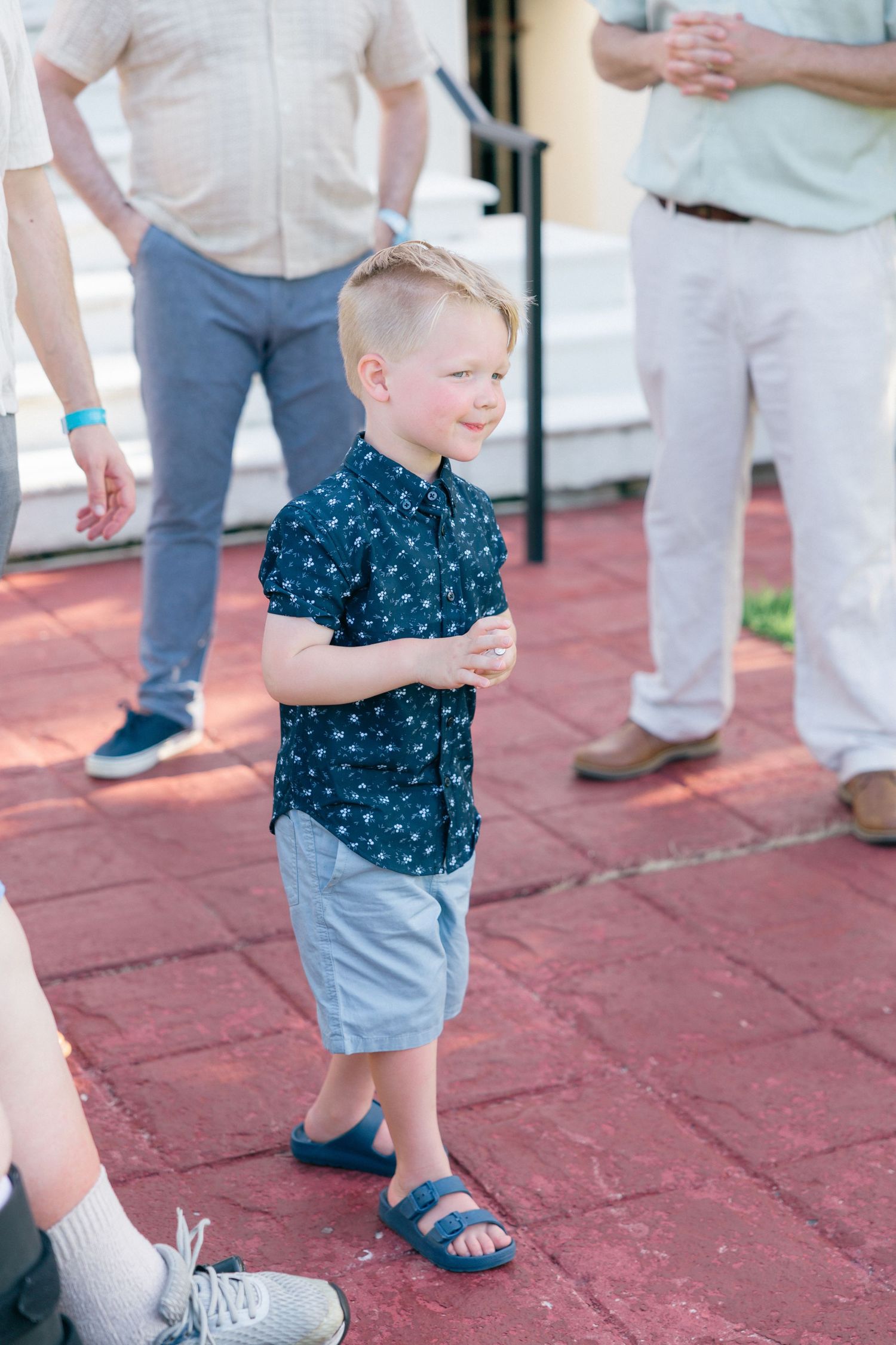 Small child in blue polka dot shirt and shorts walking on red brick pavement.