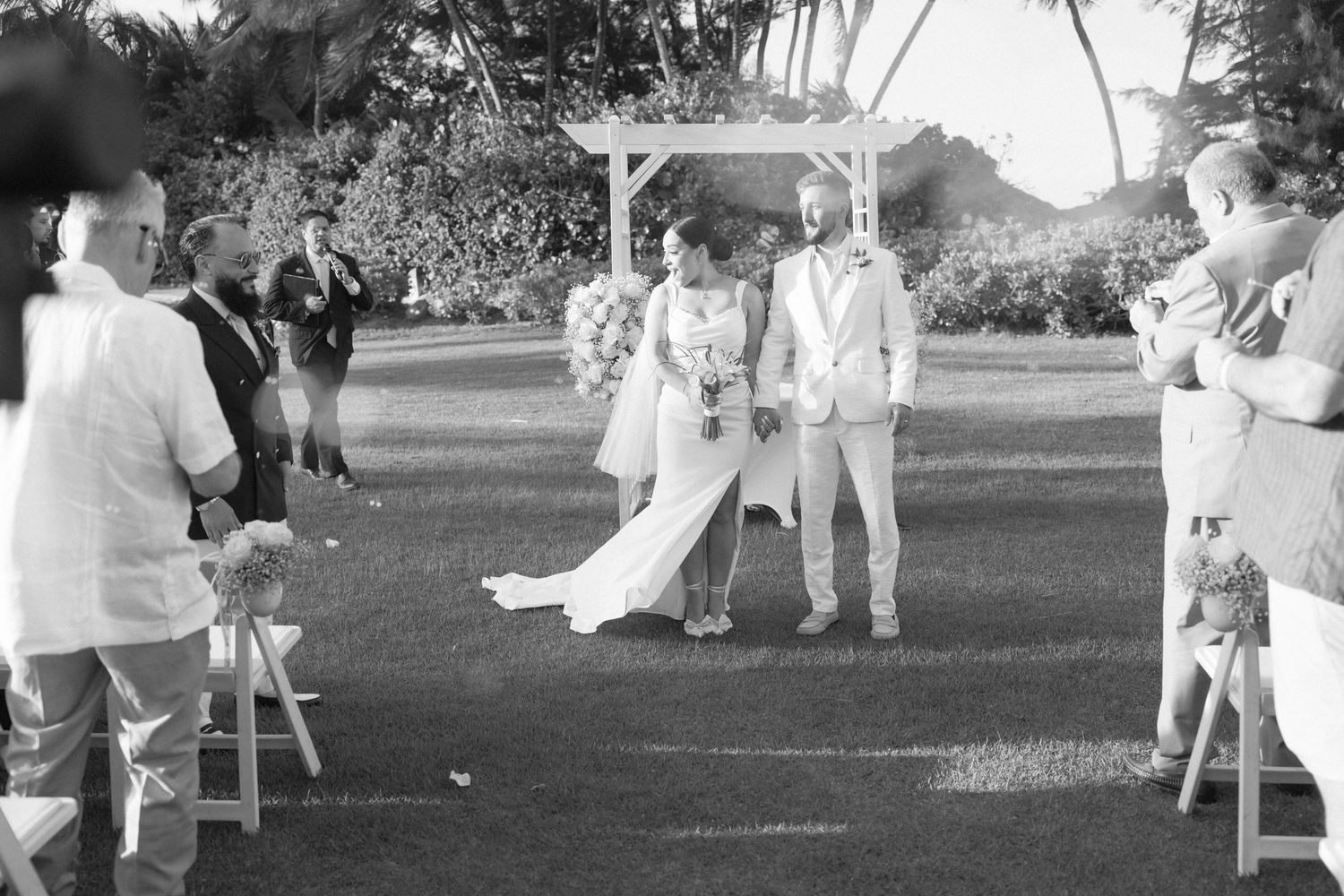 Wide view of outdoor wedding ceremony with guests seated on white chairs.