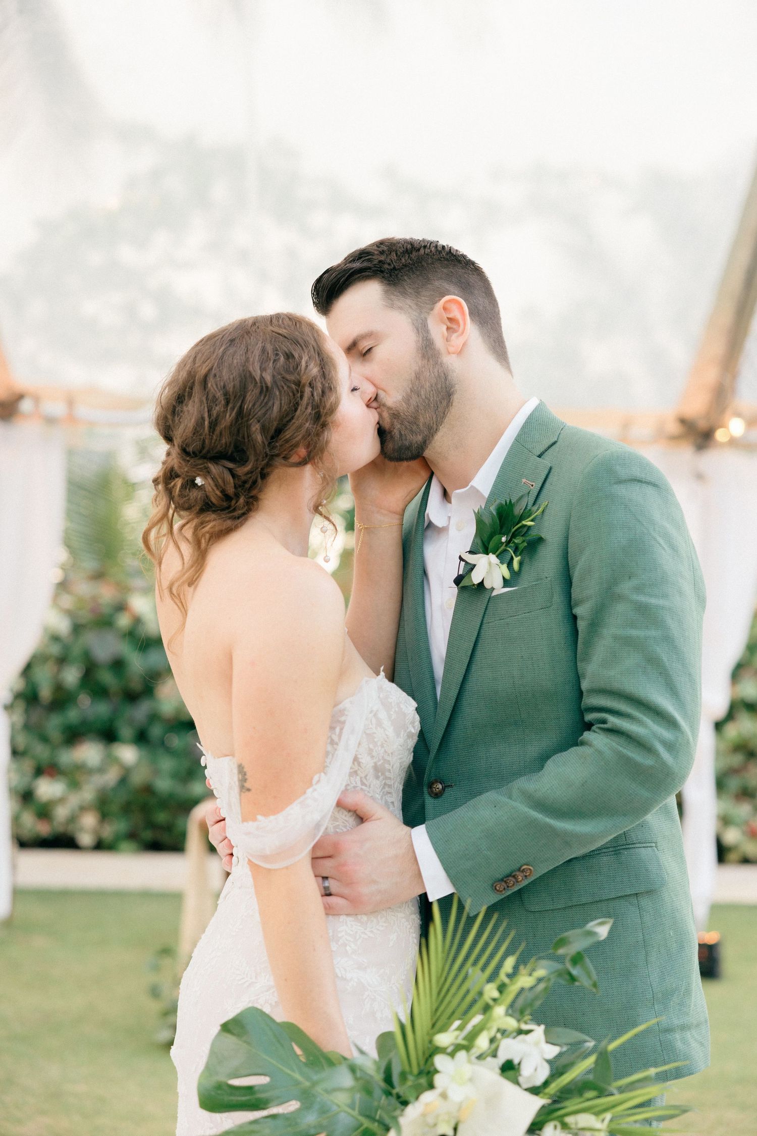 A romantic wedding moment captured in a lush garden setting with tropical greenery.
