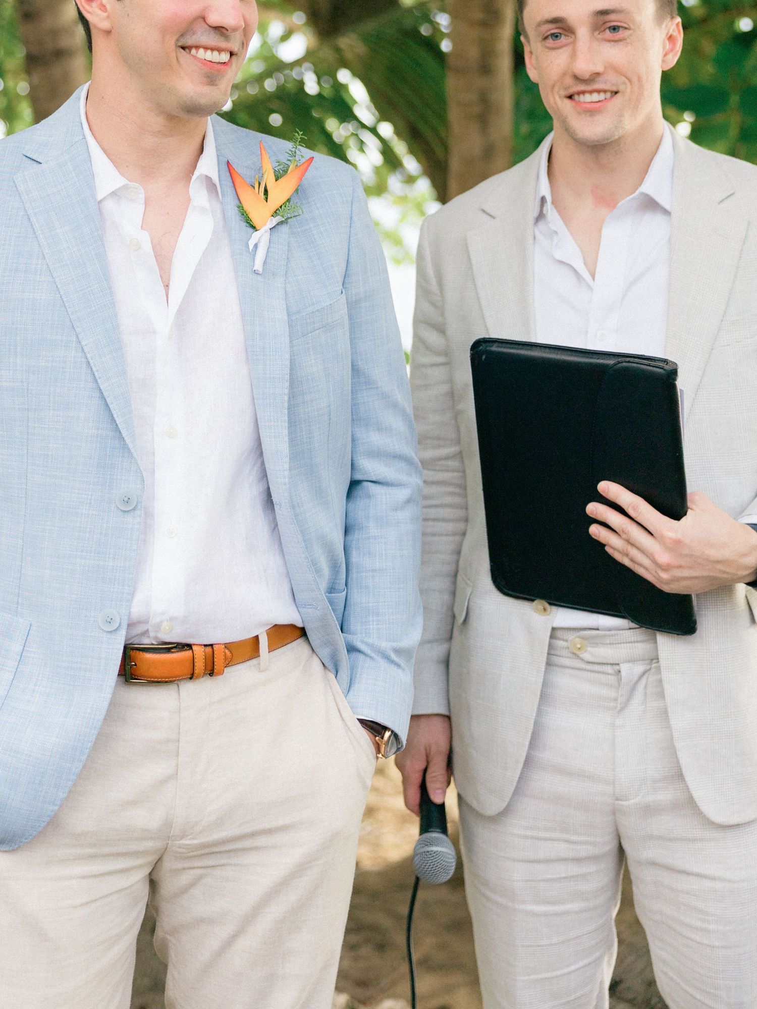 Groomsmen in light blue and white suits stand together during outdoor ceremony.