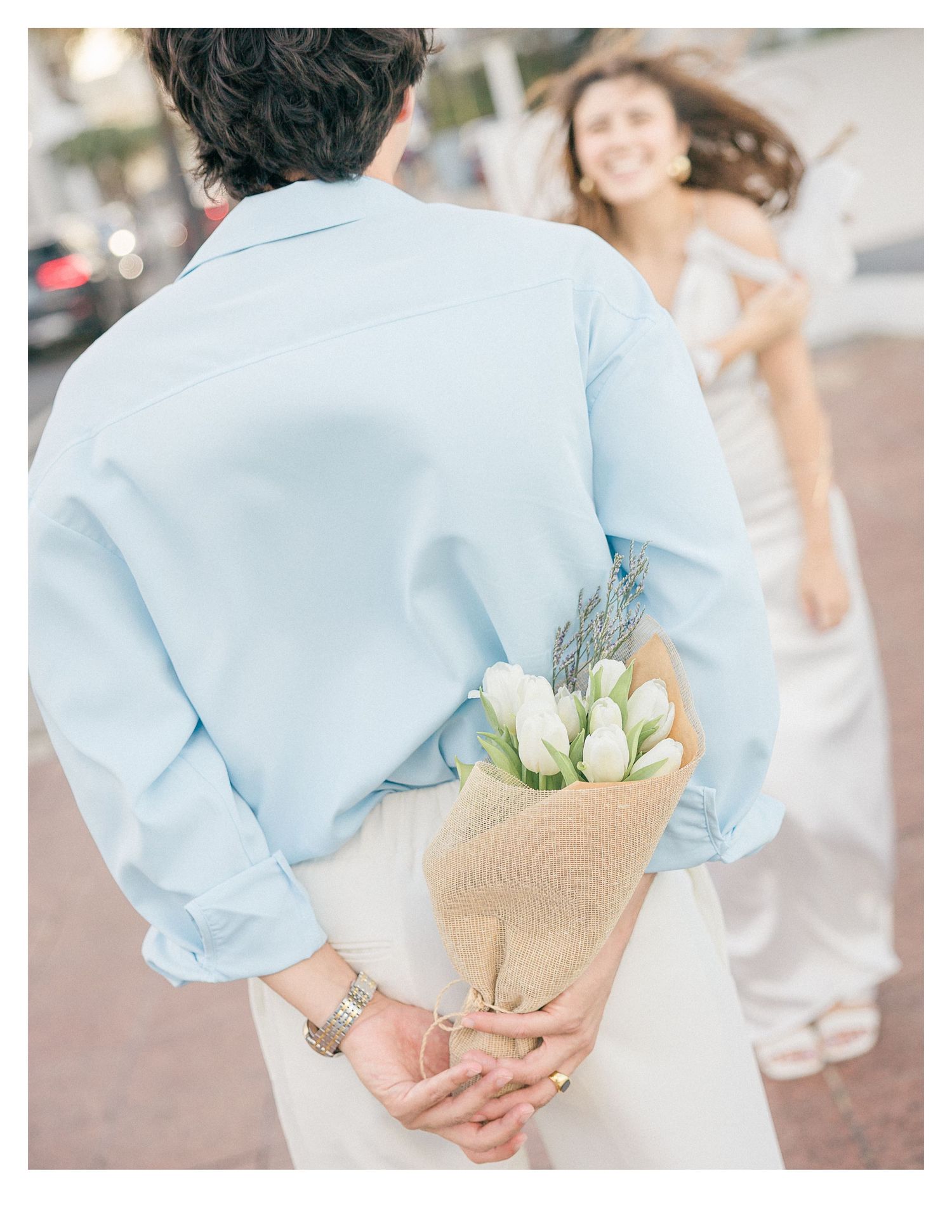 Person in light blue shirt holding a hidden bouquet of flowers behind their back.