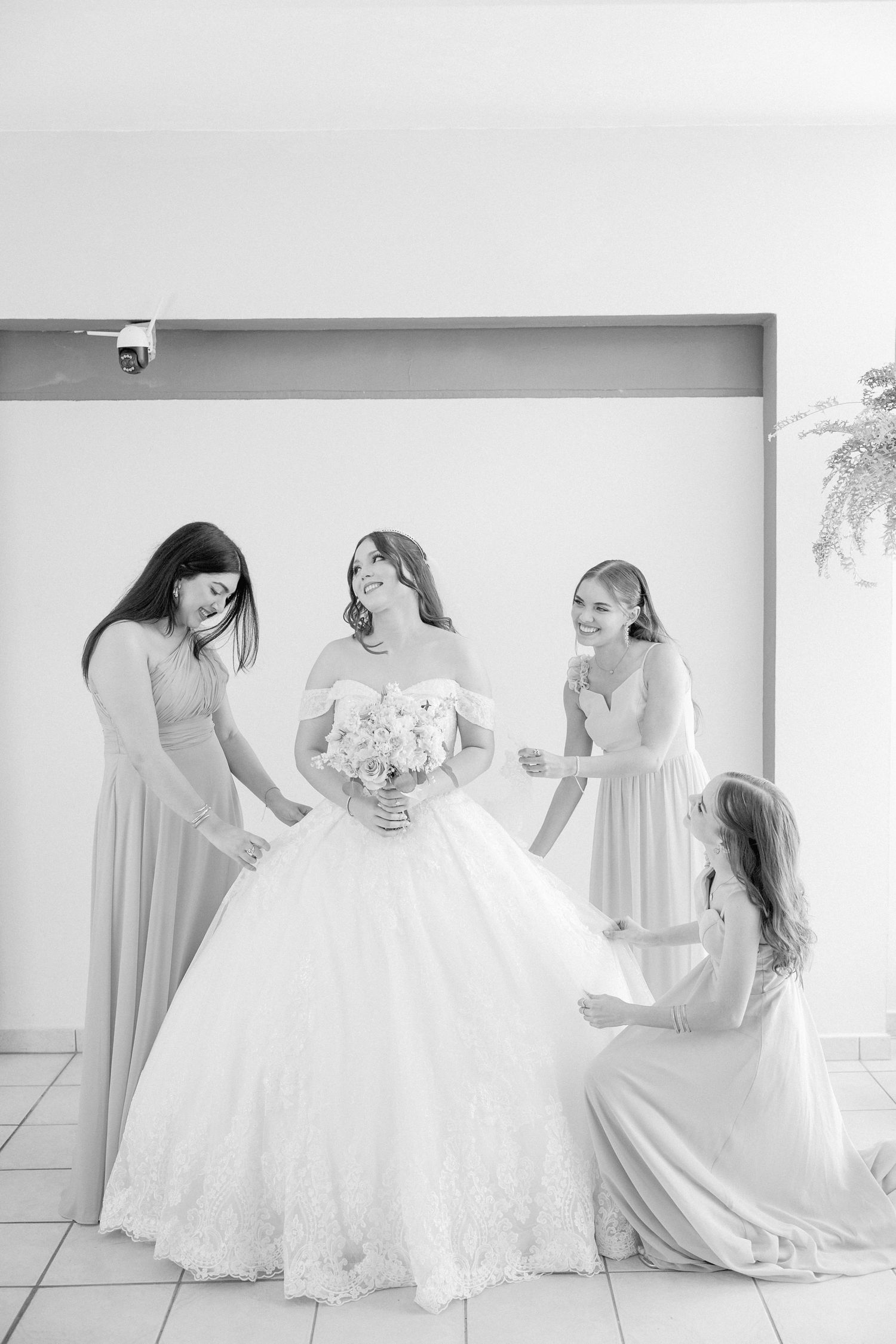 Black and white photo of bridesmaids helping with a full wedding gown.