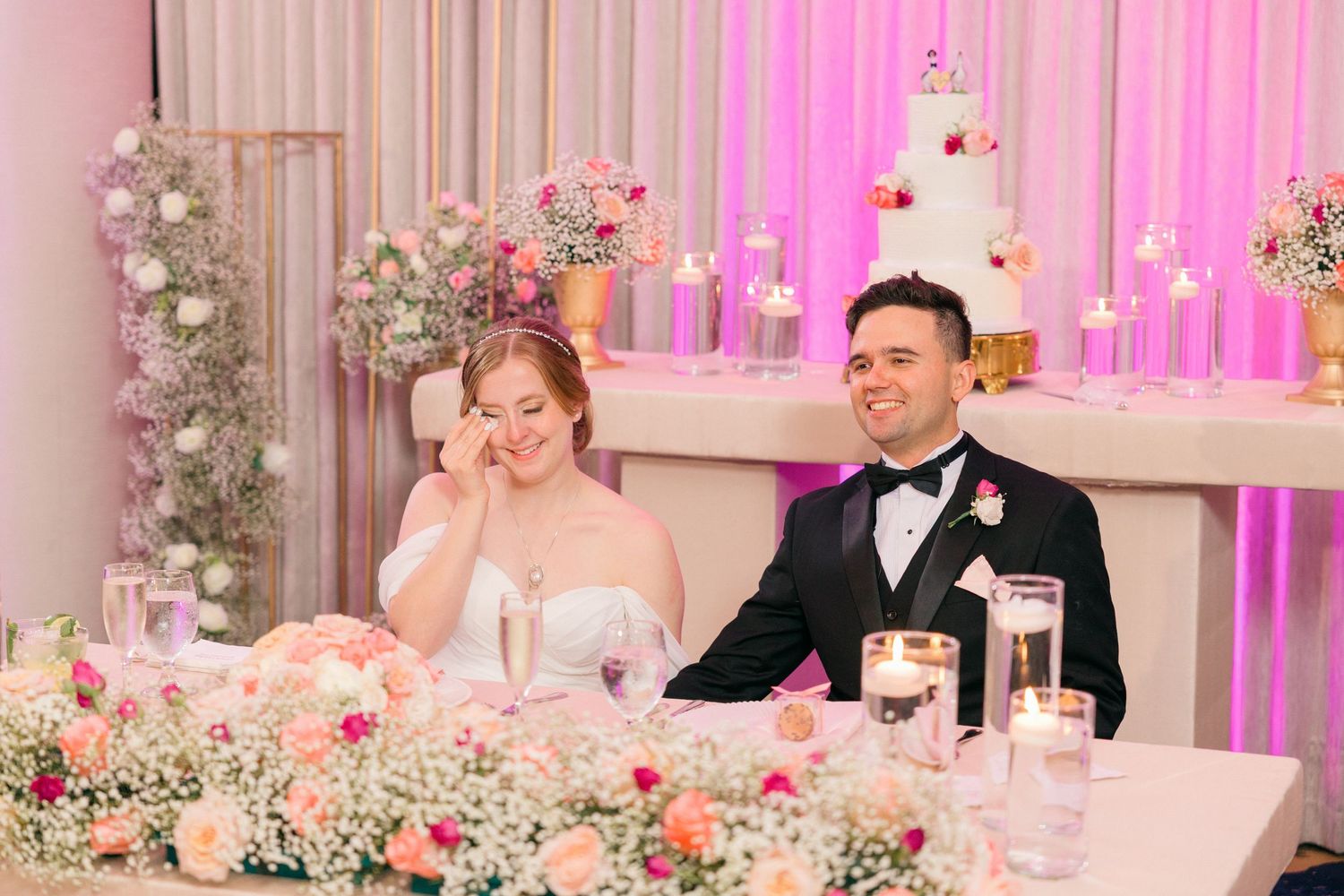 Wedding reception venue with pink lighting and romantic floral table decorations.