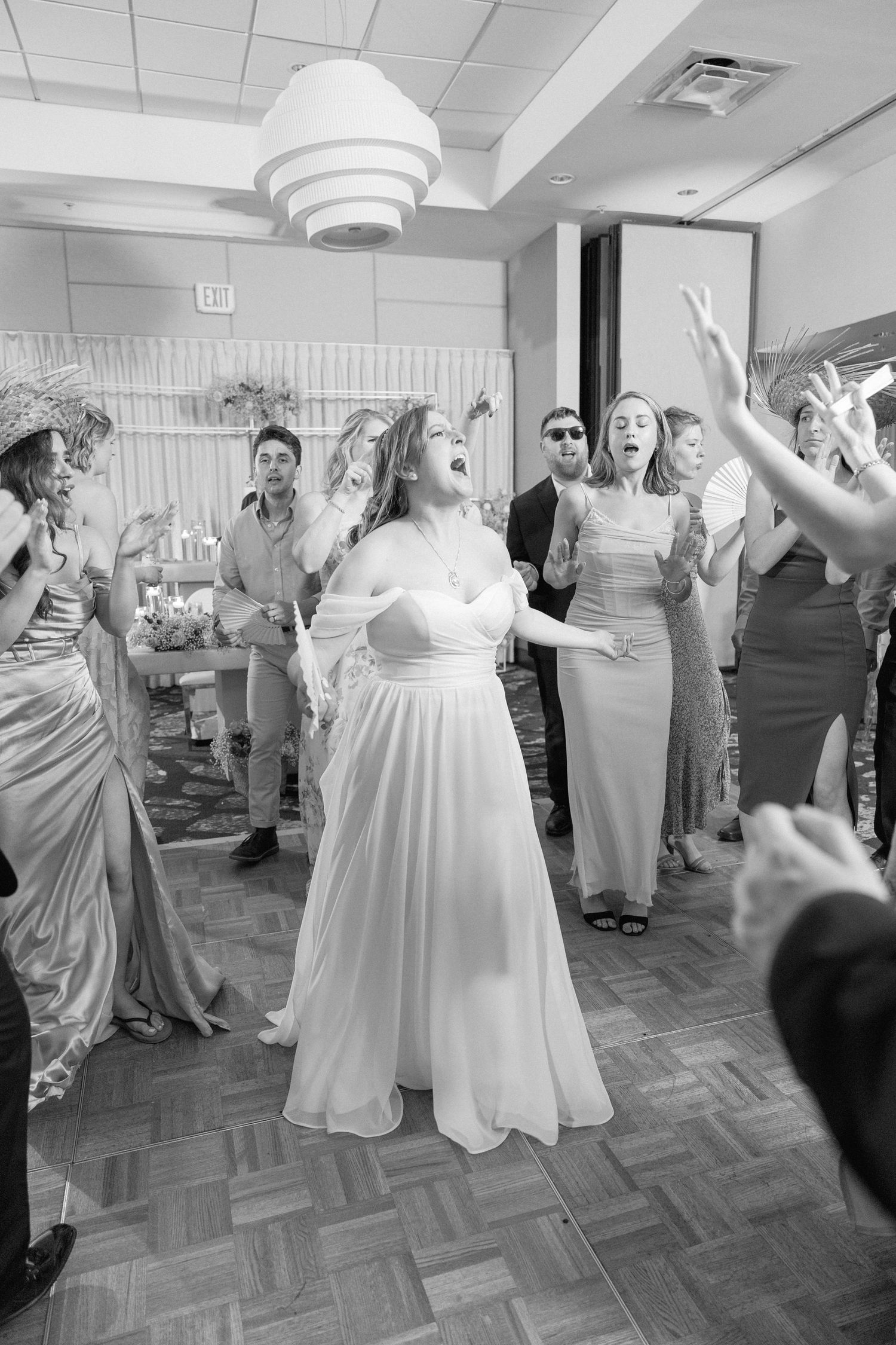 Wedding guests dance and celebrate in a reception hall with white decor and patterned flooring.