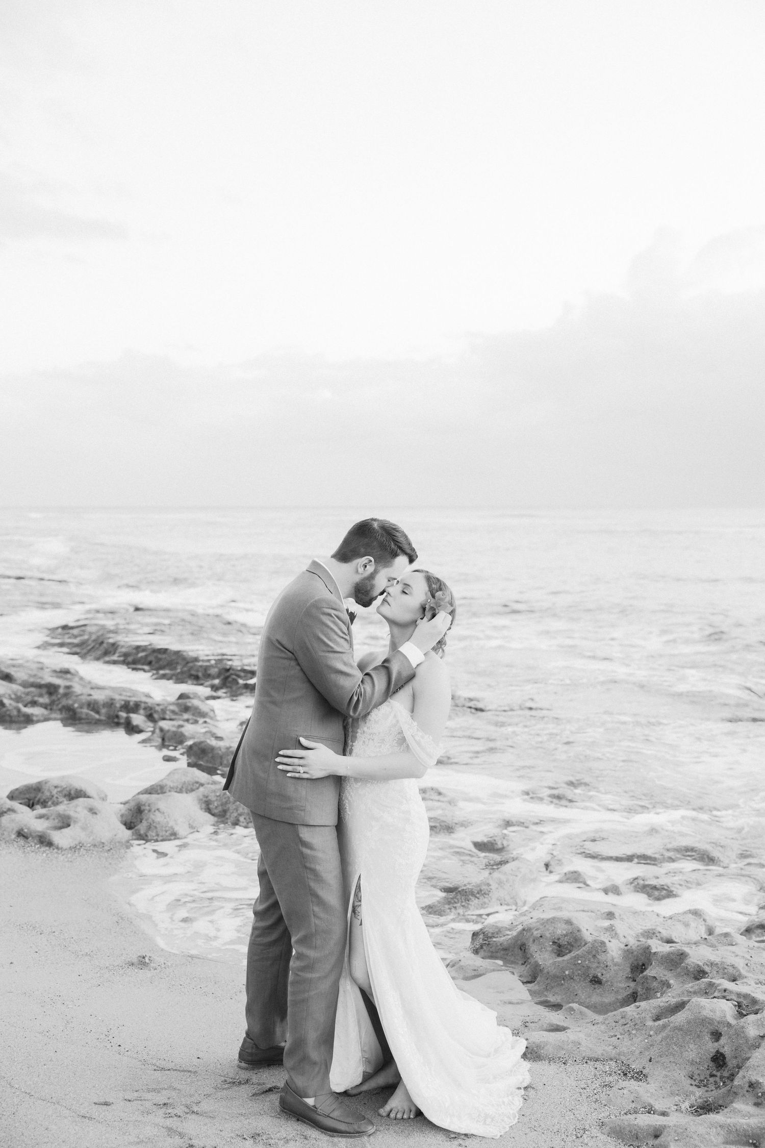 Couple embracing on a rocky beach during sunset.
