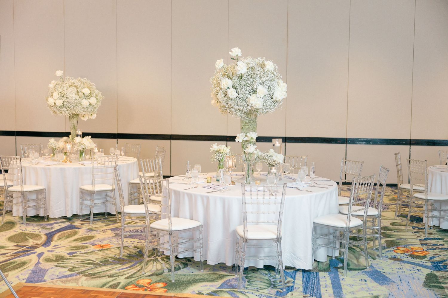 Modern ballroom with white round tables and crystal chandeliers set for an elegant event.