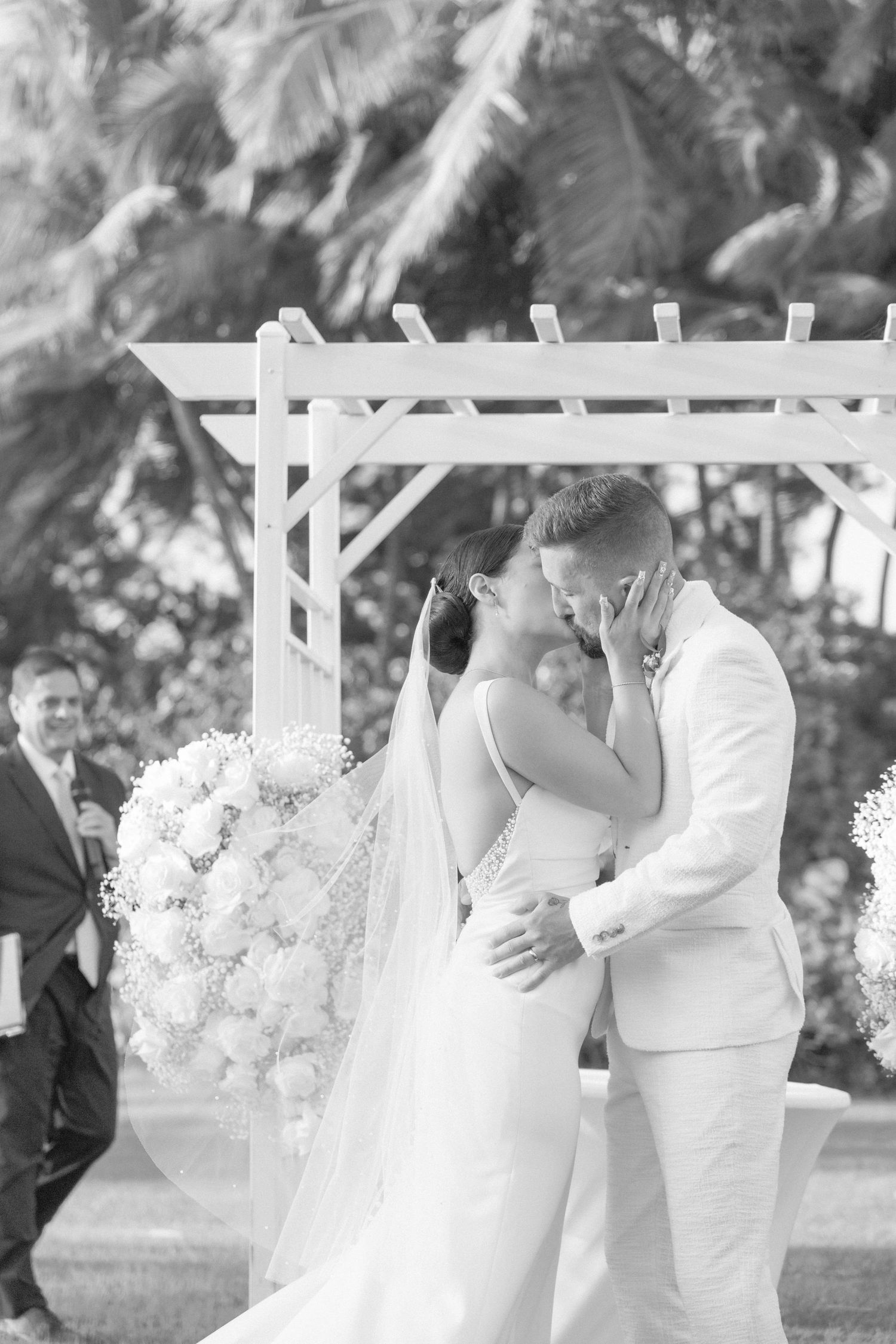Black and white wedding photograph under decorated arbor with elegant floral arrangements.