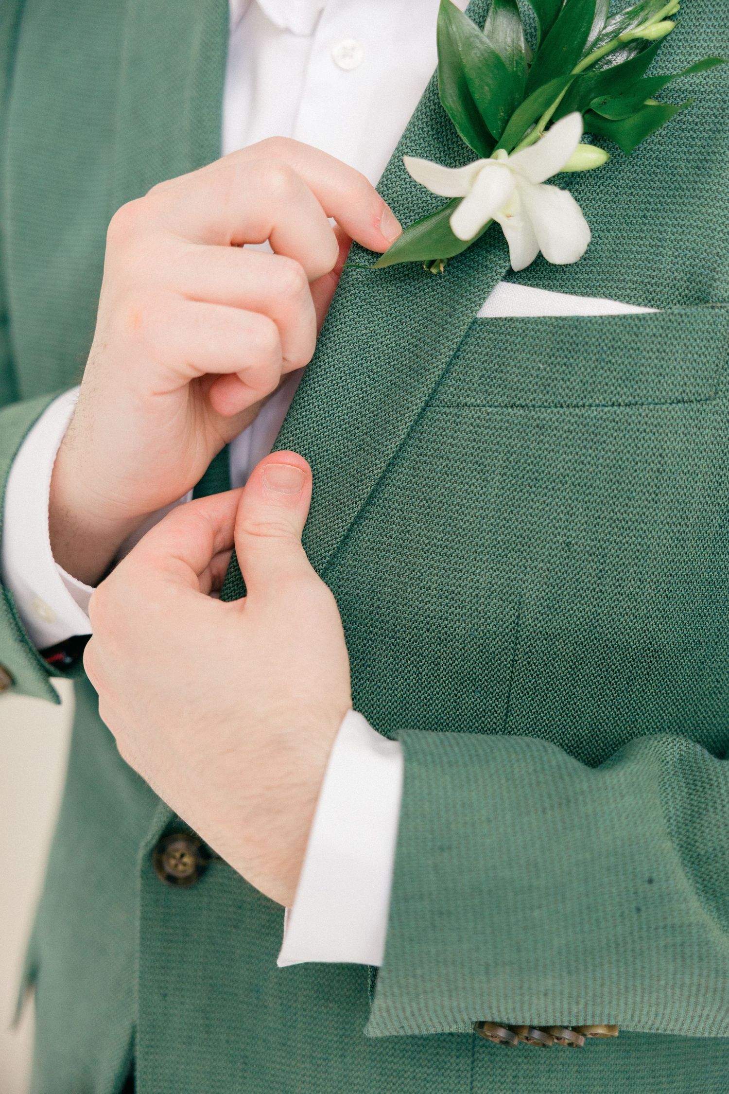 Close-up shots of hands adjusting a white boutonniere flower on a green suit jacket.