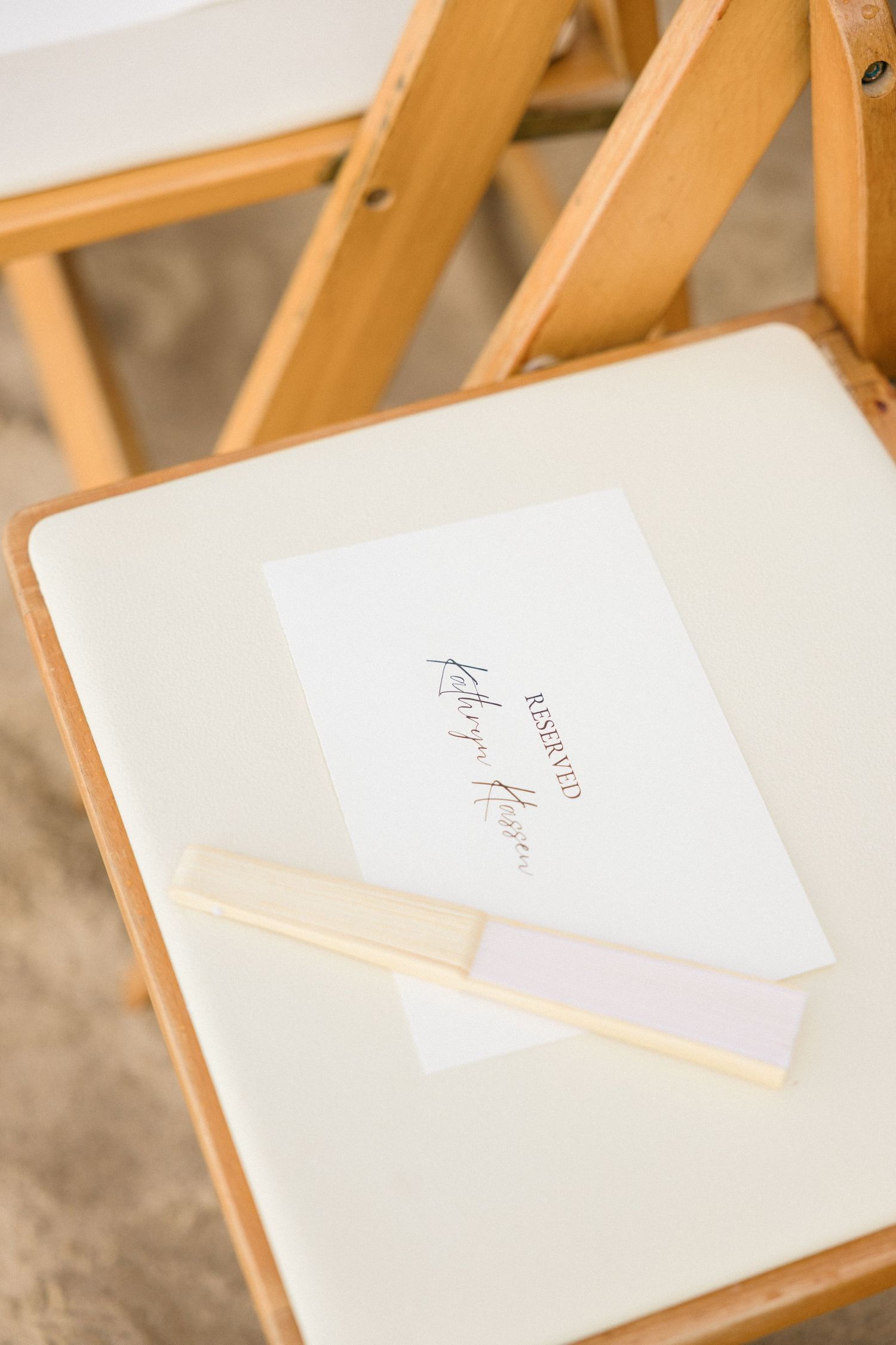 White wedding ceremony programs placed on wooden folding chairs.