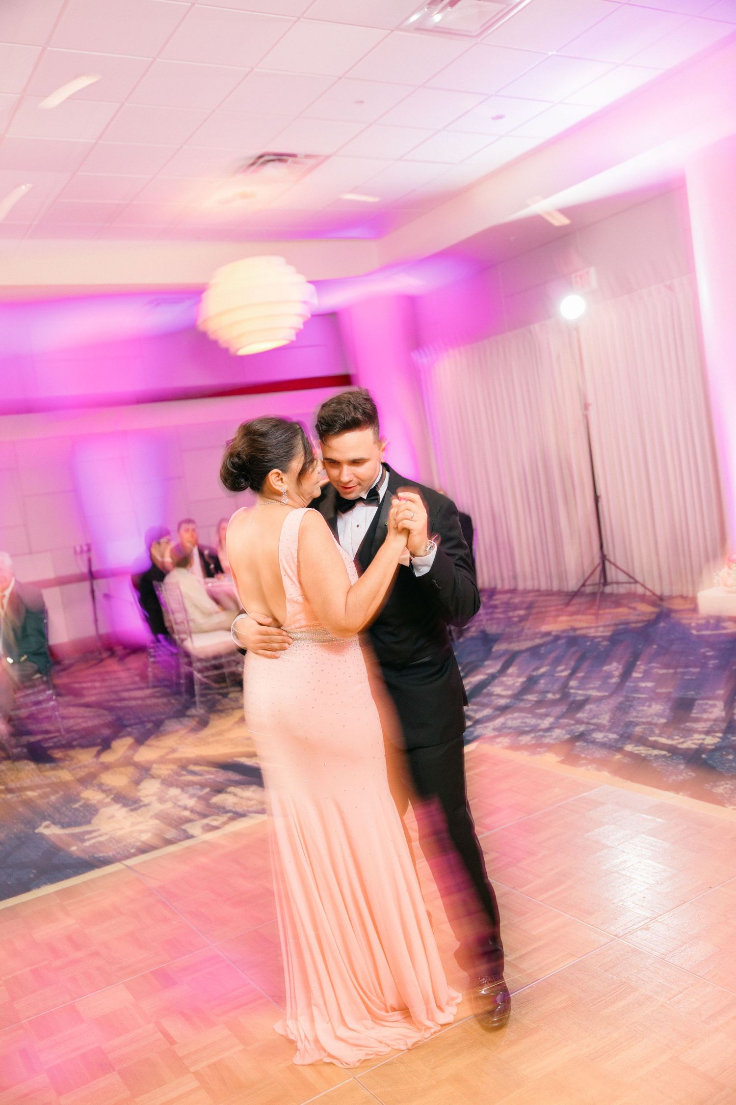 Couple sharing a romantic dance under pink lighting at their wedding reception.