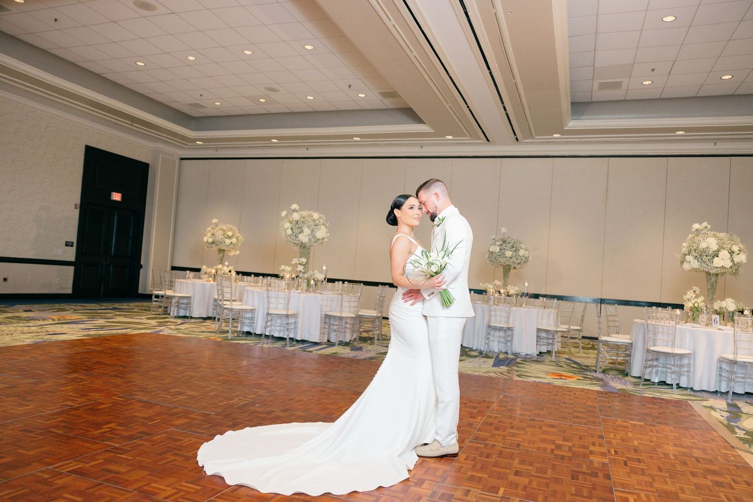 Wedding reception venue setup with elegant white decor and floral arrangements in a spacious ballroom.