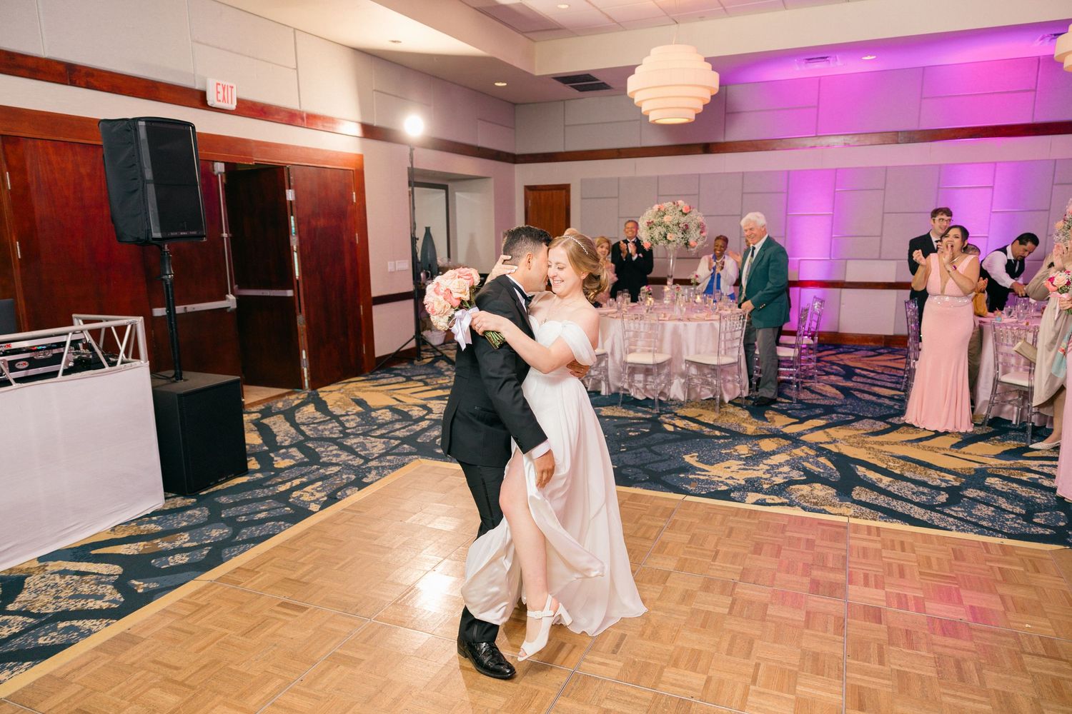 Couple dancing together in a ballroom with purple uplighting and a decorative patterned carpet.