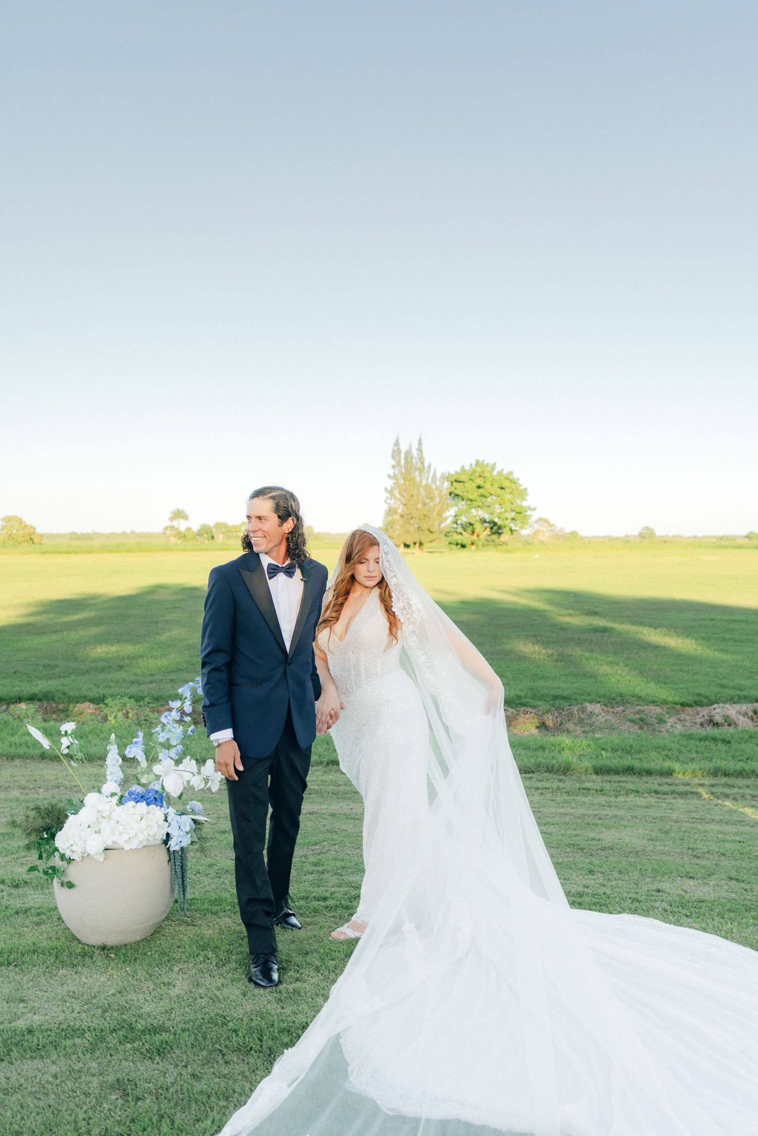 Bride and groom share a romantic moment on rolling green hills at sunset.