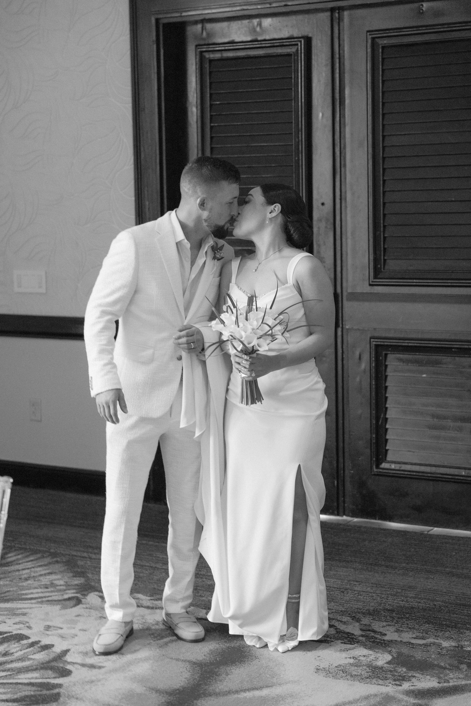 A romantic black and white wedding portrait of a couple in matching white attire.