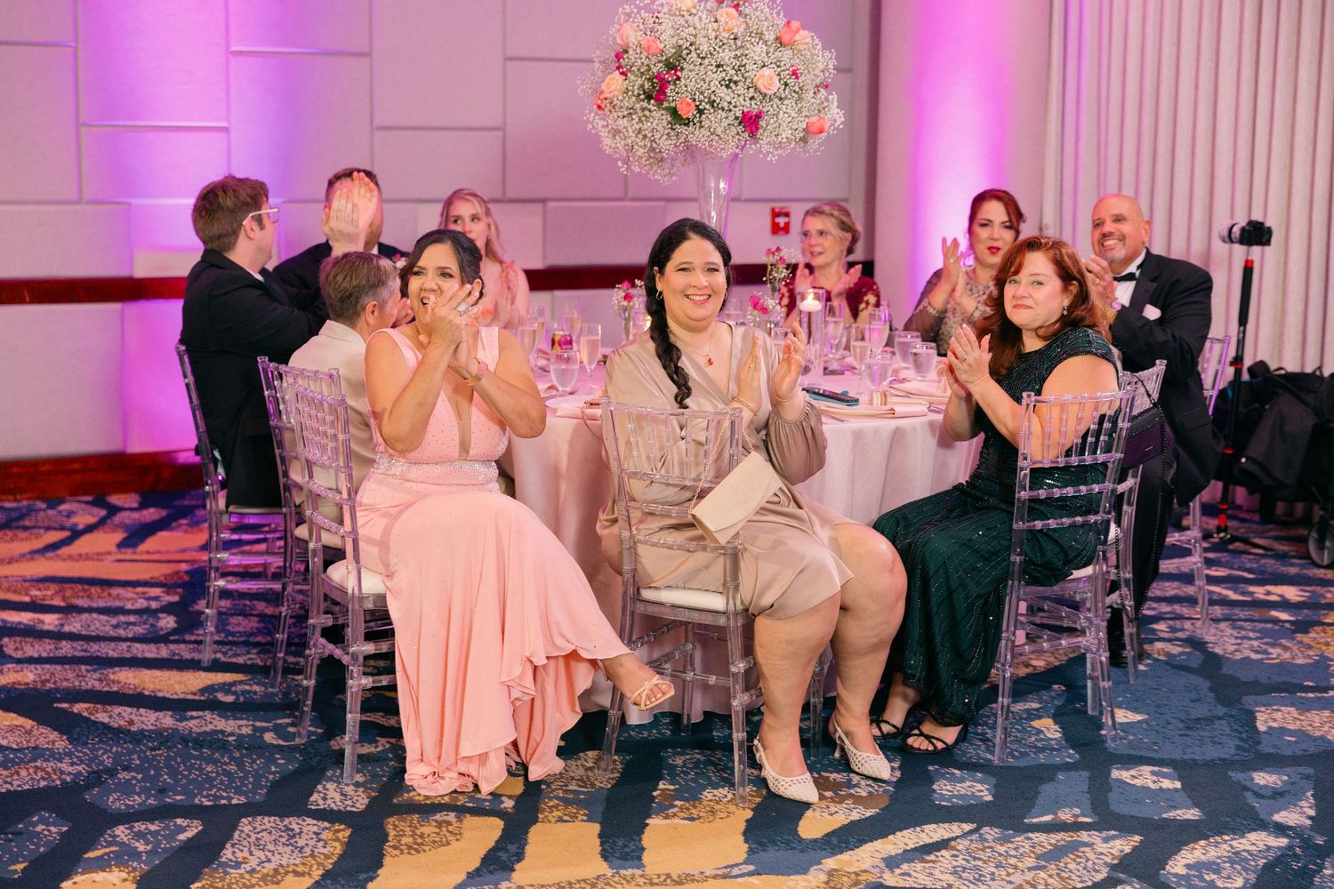 Pink-lit ballroom with elegant table settings and floral arrangements for a wedding reception.