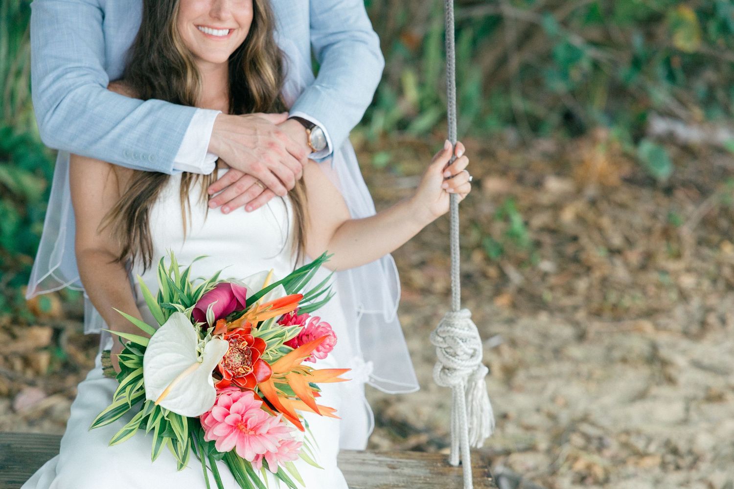 A vibrant tropical bouquet with orange birds of paradise flowers and pink blooms against a natural outdoor setting.