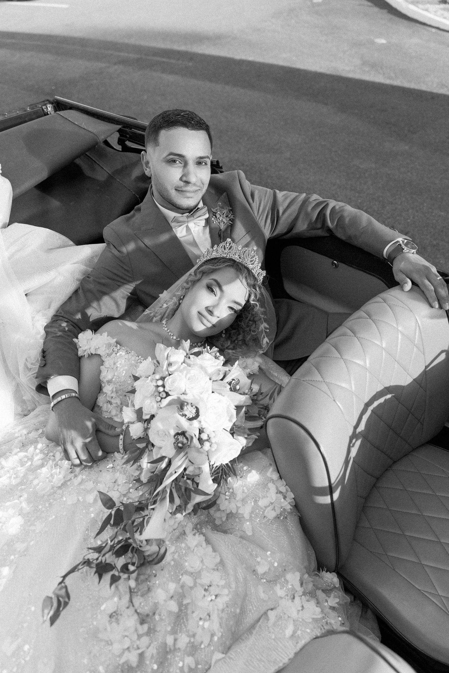 Wedding couple poses artistically on gray couch with flowing dress and flowers.