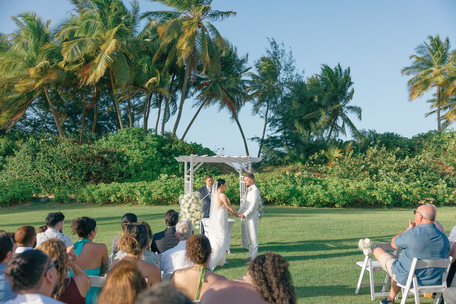 Tropical beach wedding ceremony setup with palm trees and white chairs.