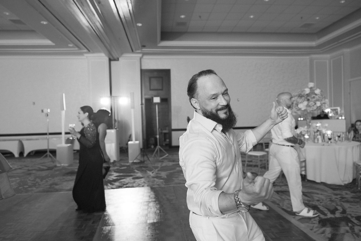 Wedding guests dancing and mingling in a ballroom with decorative ceiling details.