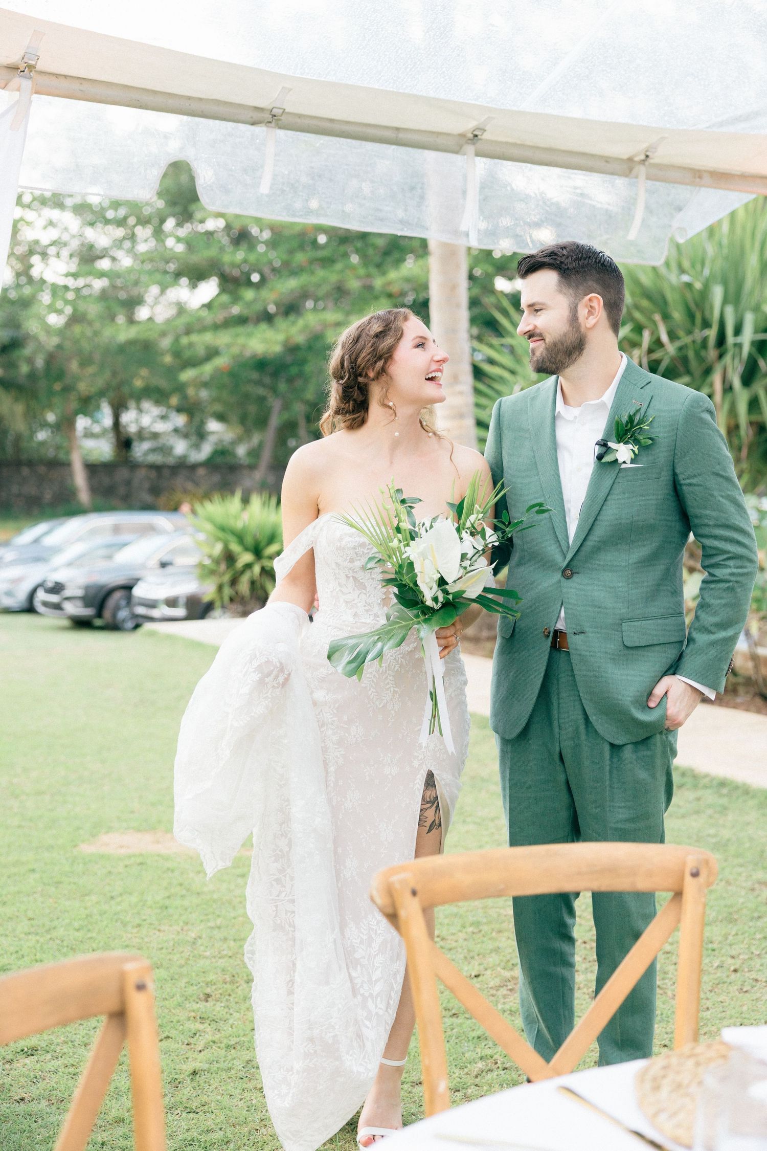 Wedding couple sharing laughs under a white tent with mountain scenery in background.