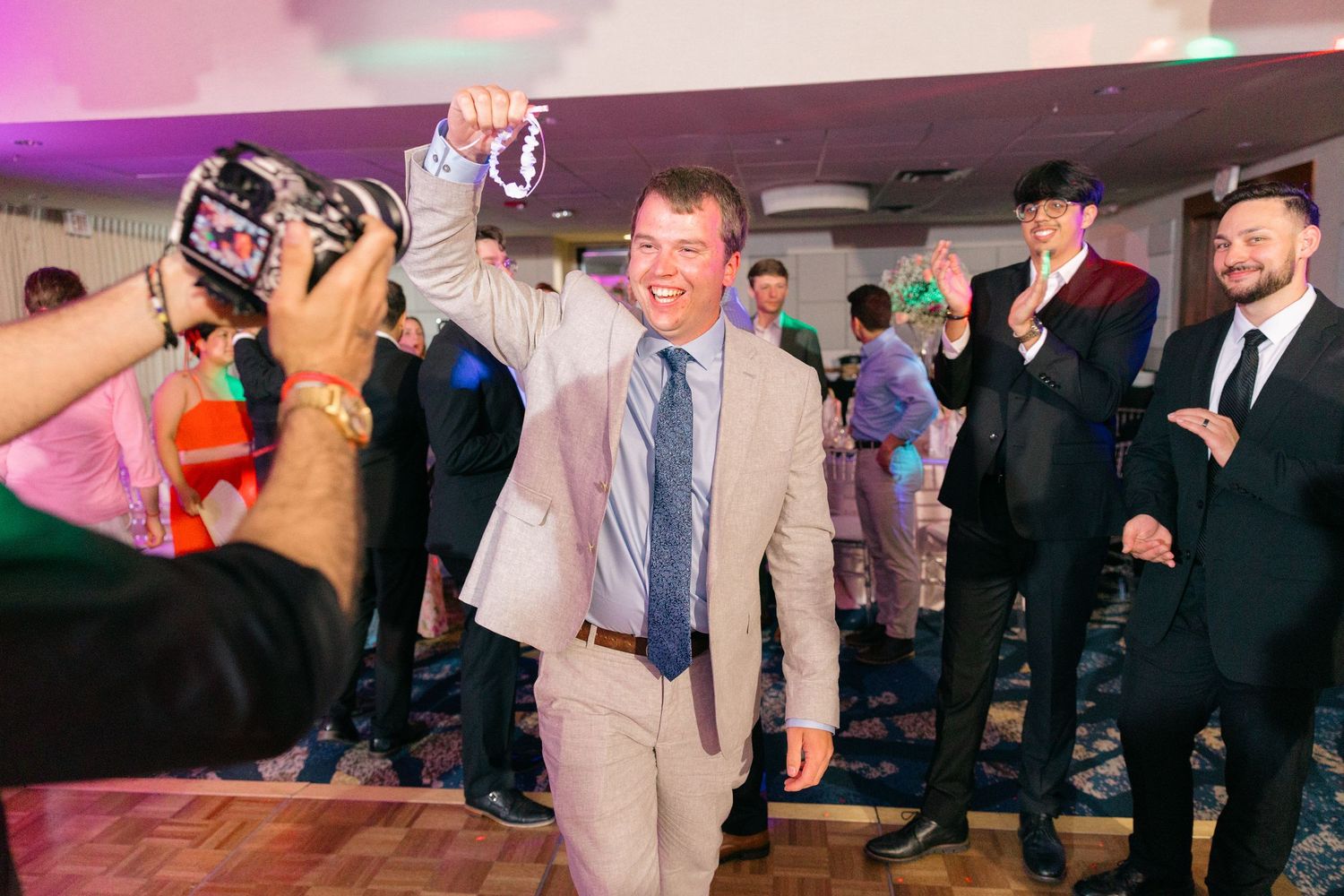 Wedding reception dance floor filled with guests celebrating under pink and purple lighting.