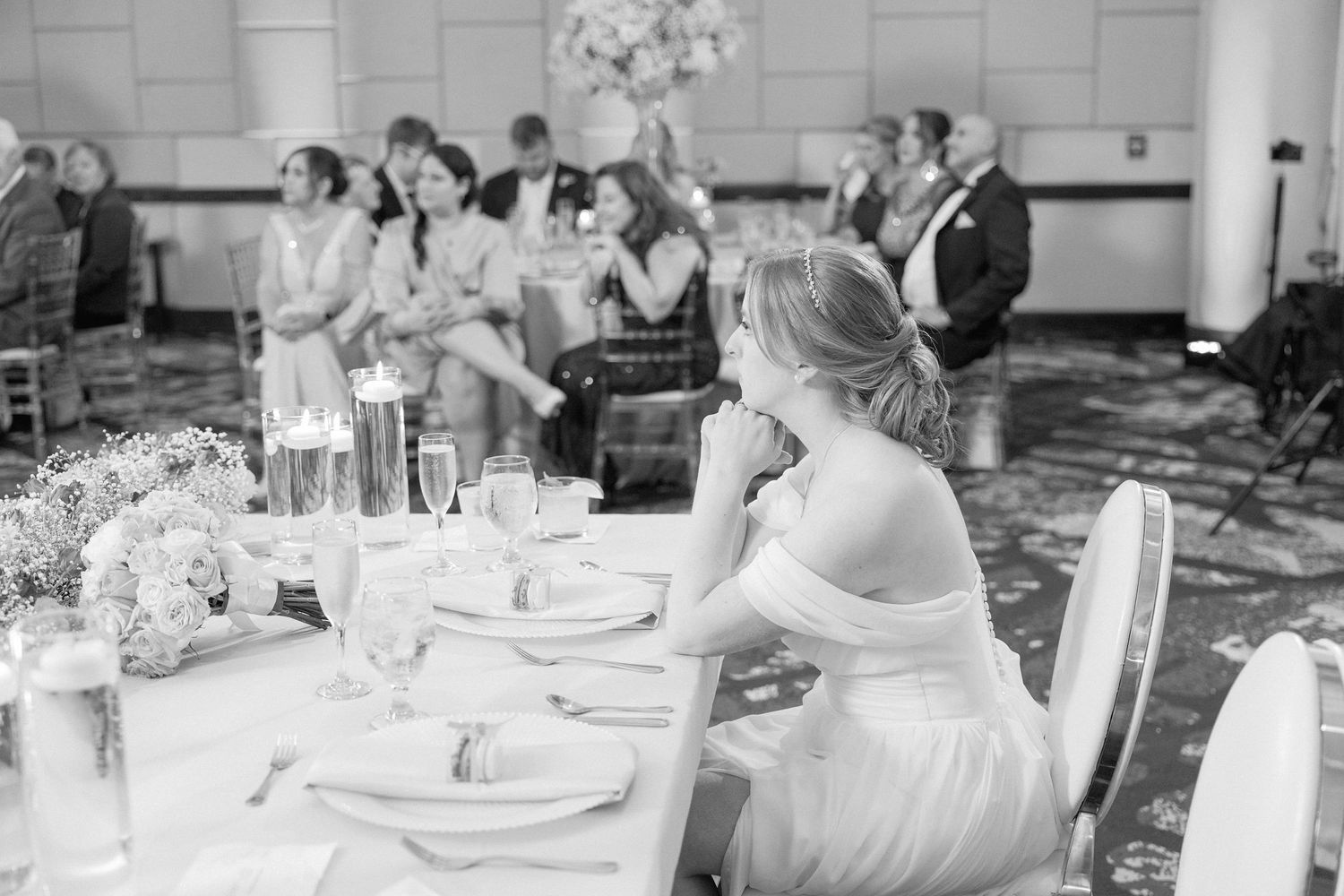 Black and white photo of wedding reception guests seated at elegantly set tables.